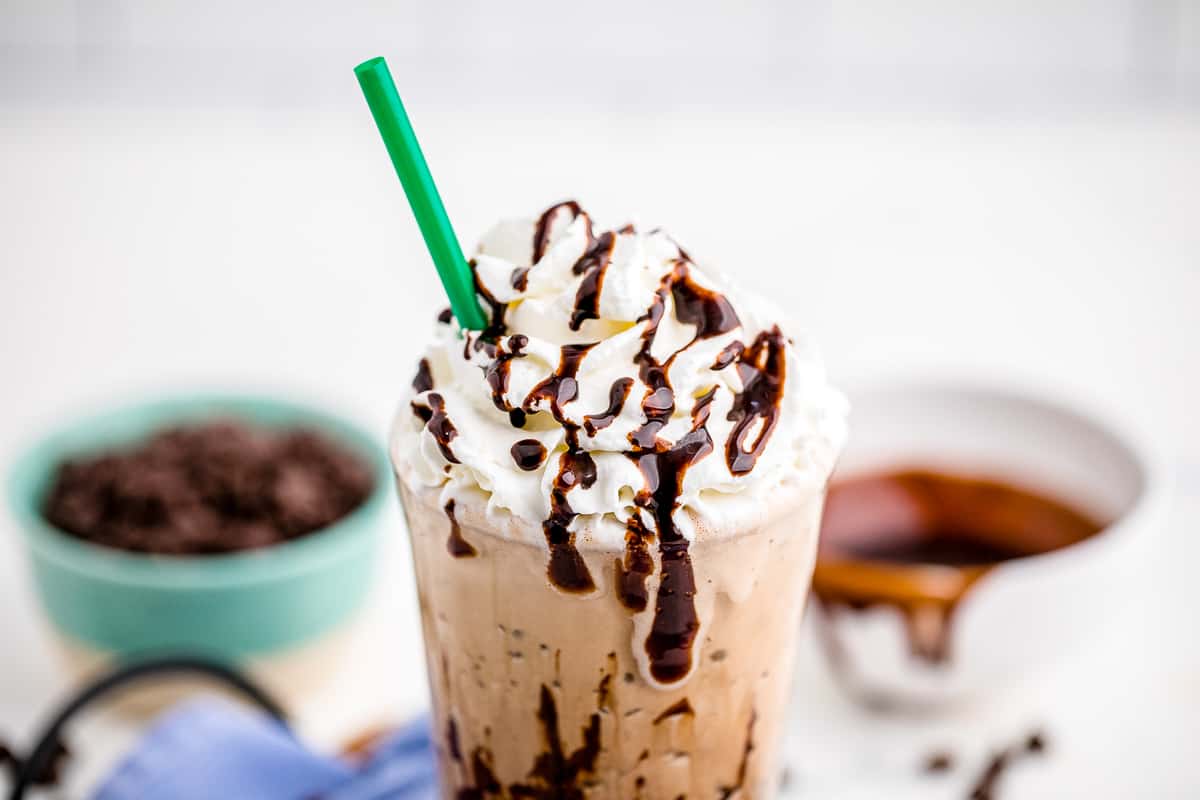 Frappuccino with whipped cream, chocolate syrup and green straw in glass