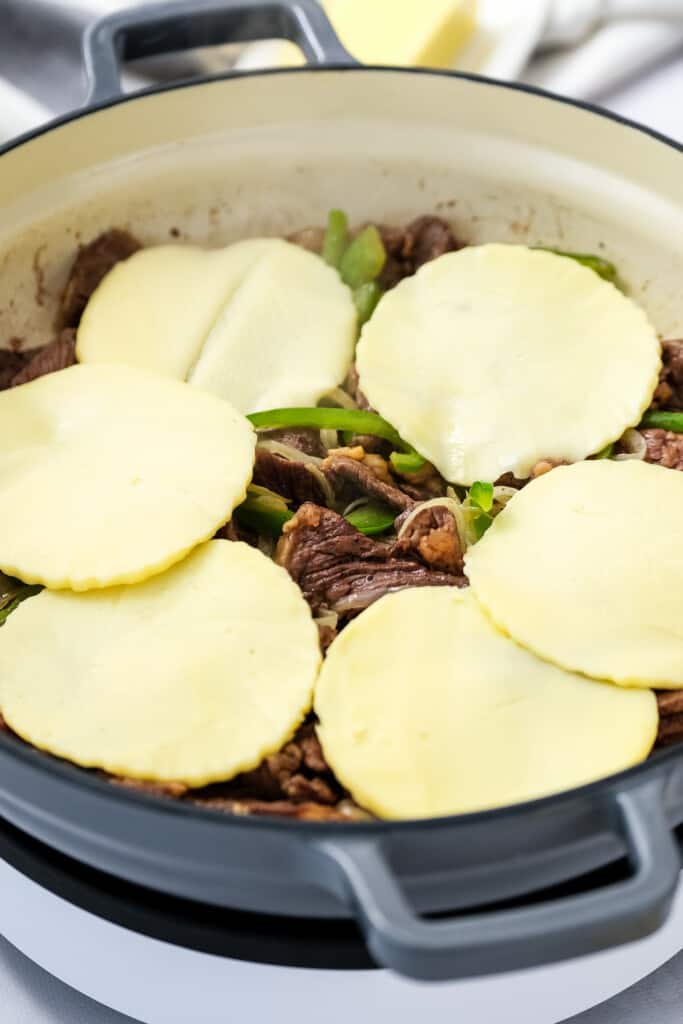 Skillet with steak strips, green peppers, onions and provolone cheese on topa