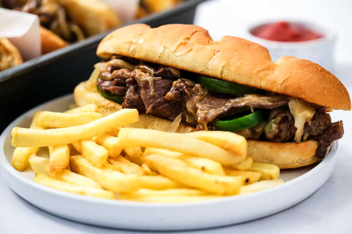 White plate with Philly Cheesesteak Sandwich and french fries