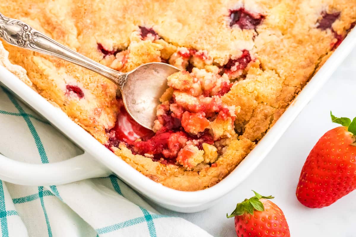 Baked strawberry dump cake in white baking dish with spoon