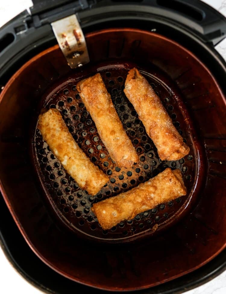 Air Fryer Basket with frozen egg rolls in it