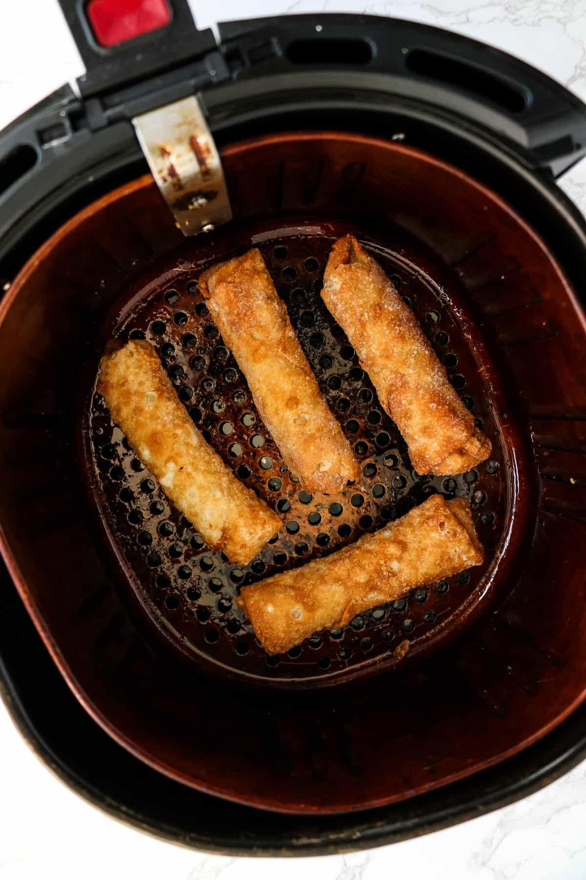 Air Fryer Basket with frozen egg rolls in it