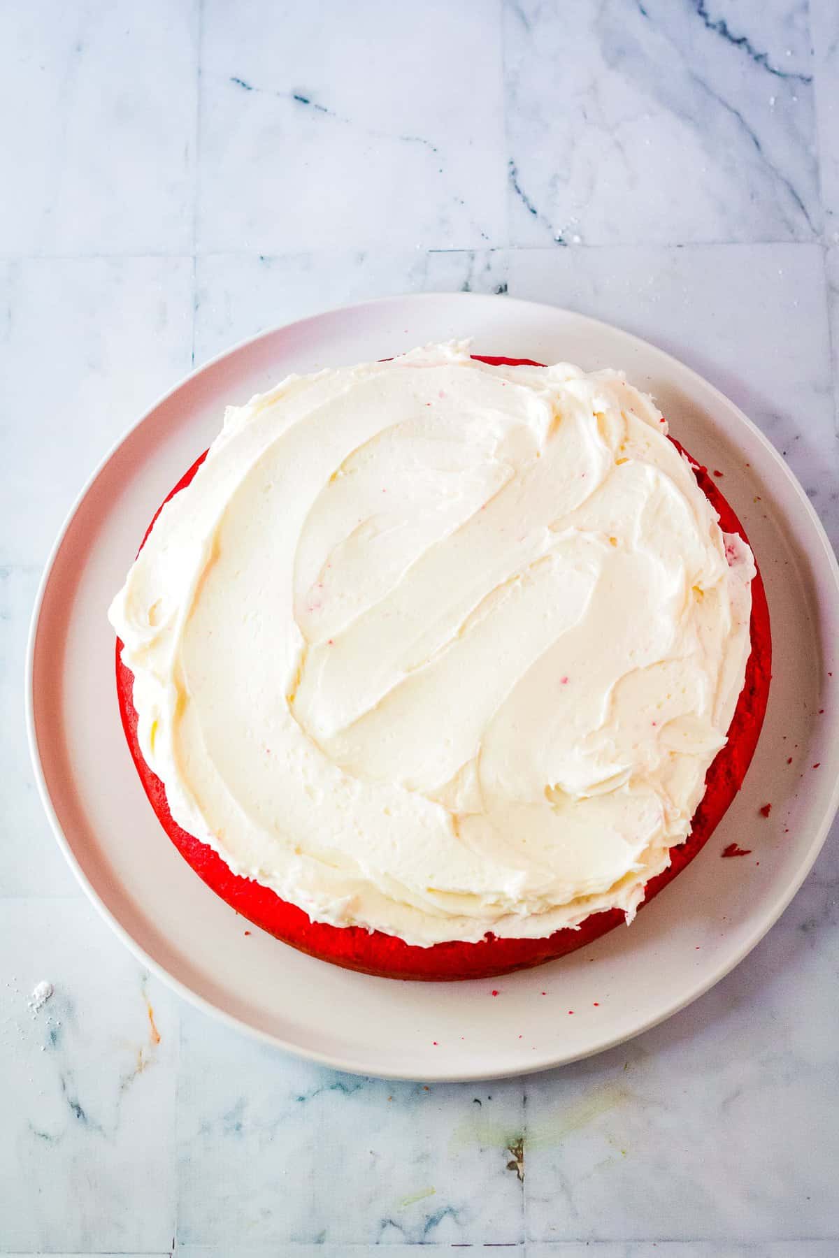 Putting buttercream frosting on top of round cake
