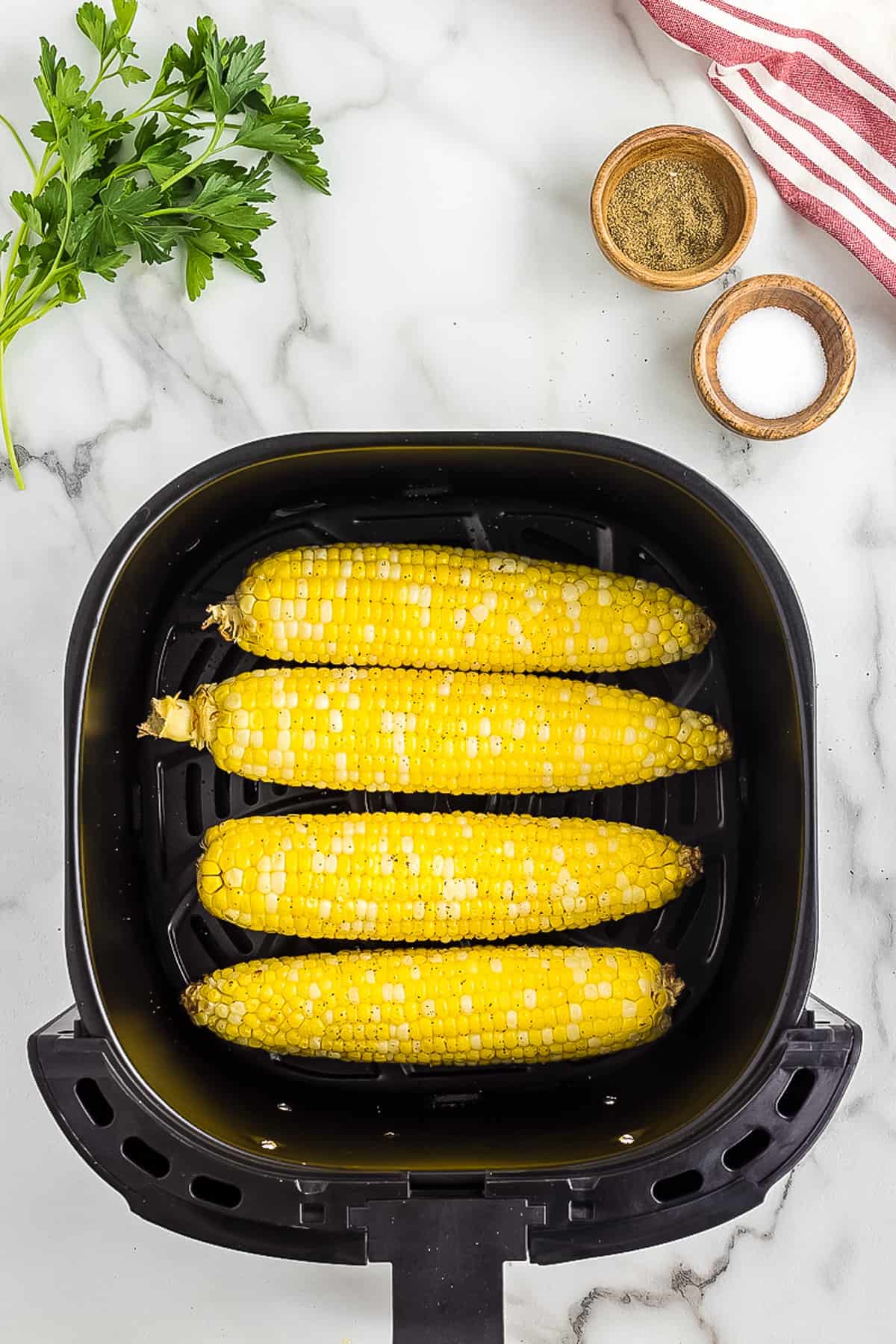 Four cooked corn cobs in air fryer basket