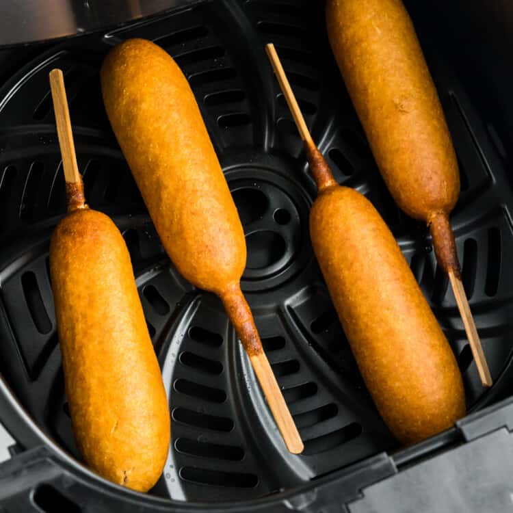 Air fryer basket with corn dogs in it