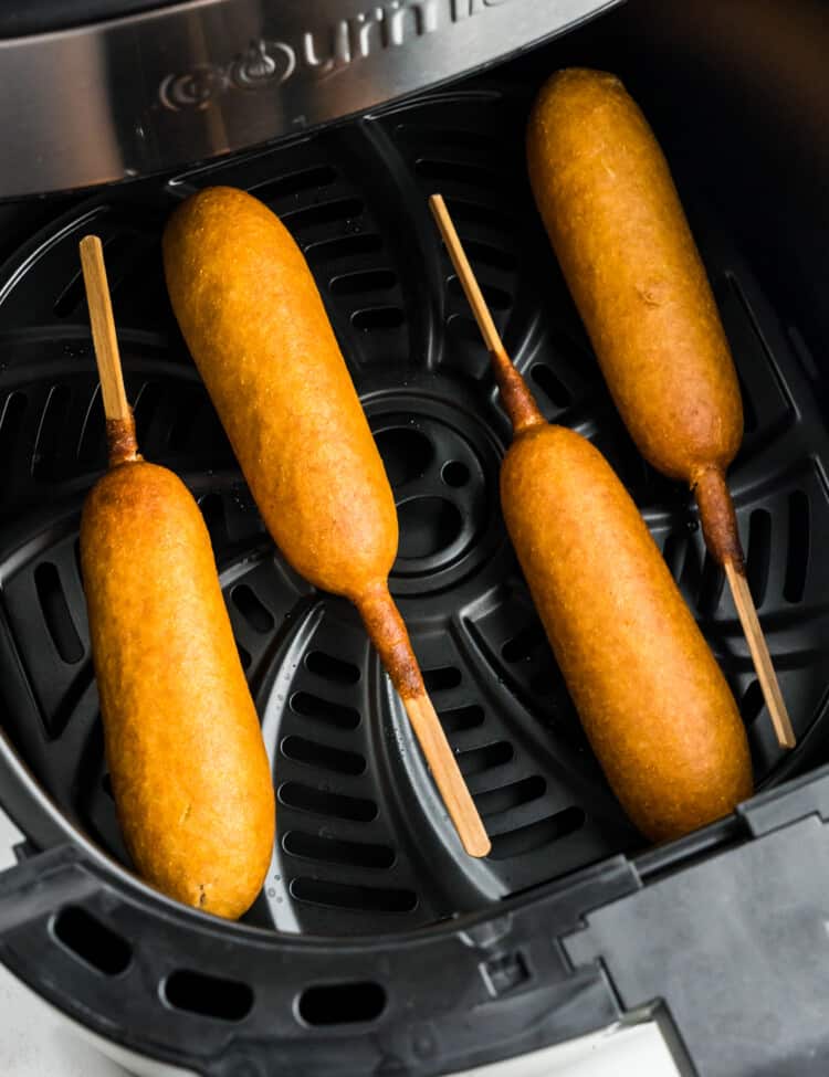 Air fryer basket with corn dogs in it