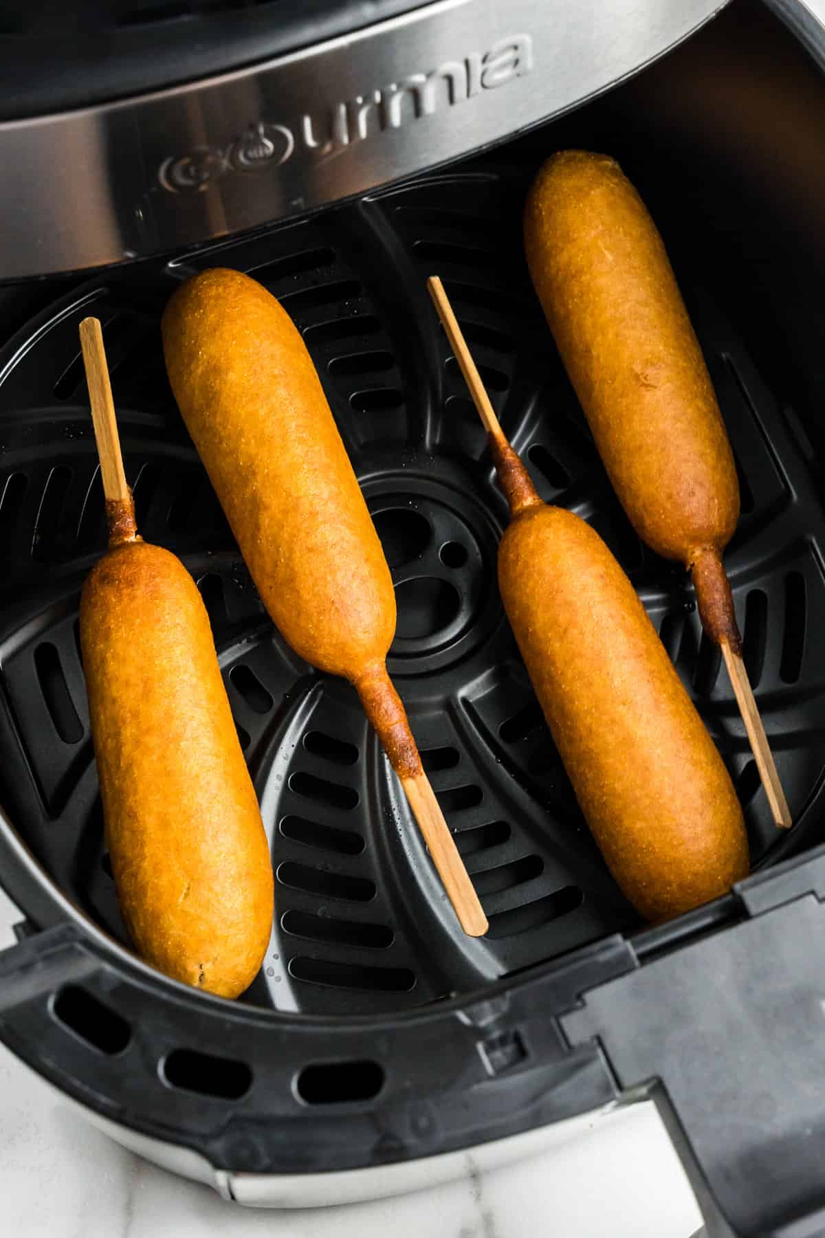 Air fryer basket with corn dogs in it