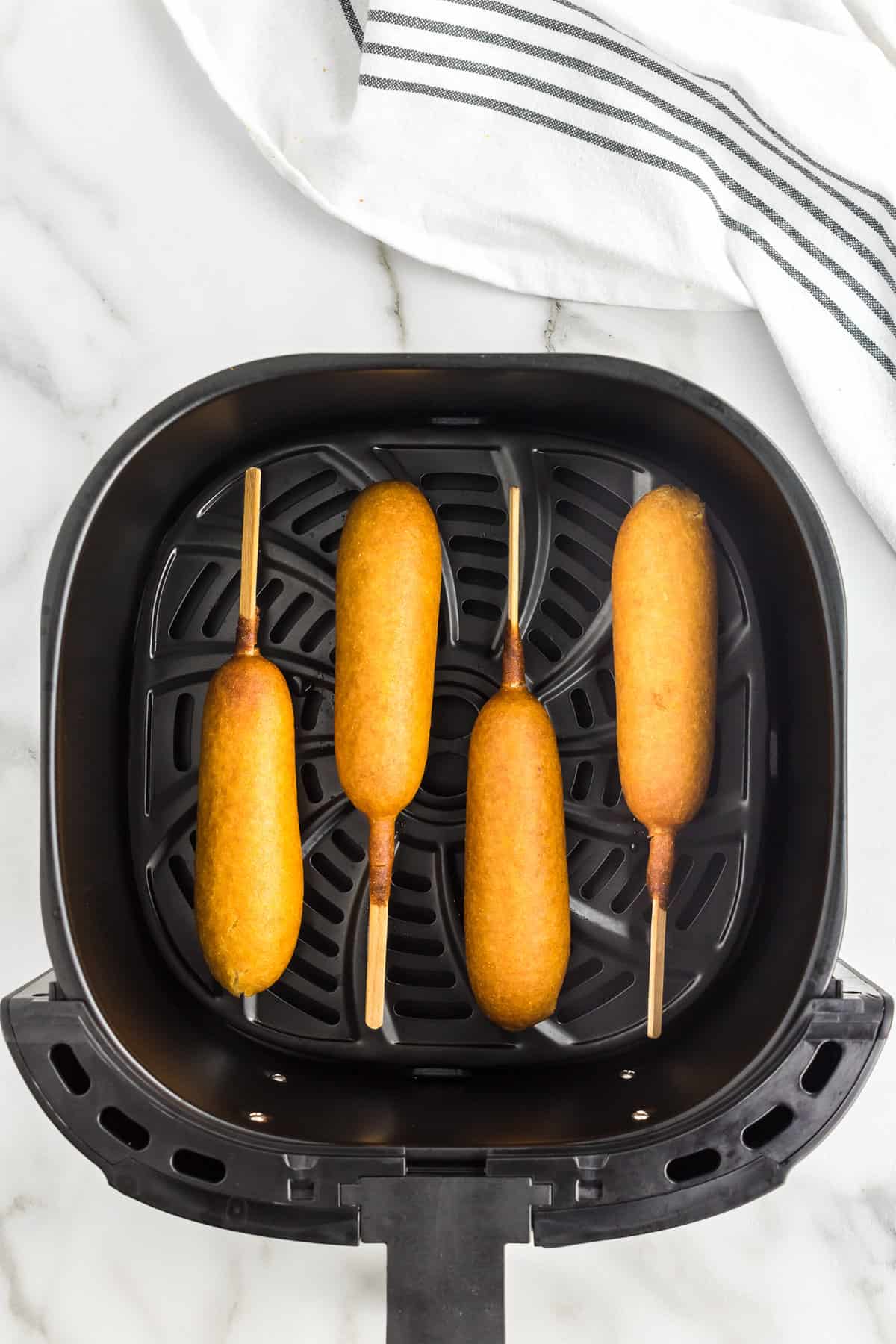 Four cooked corn dogs in air fryer basket