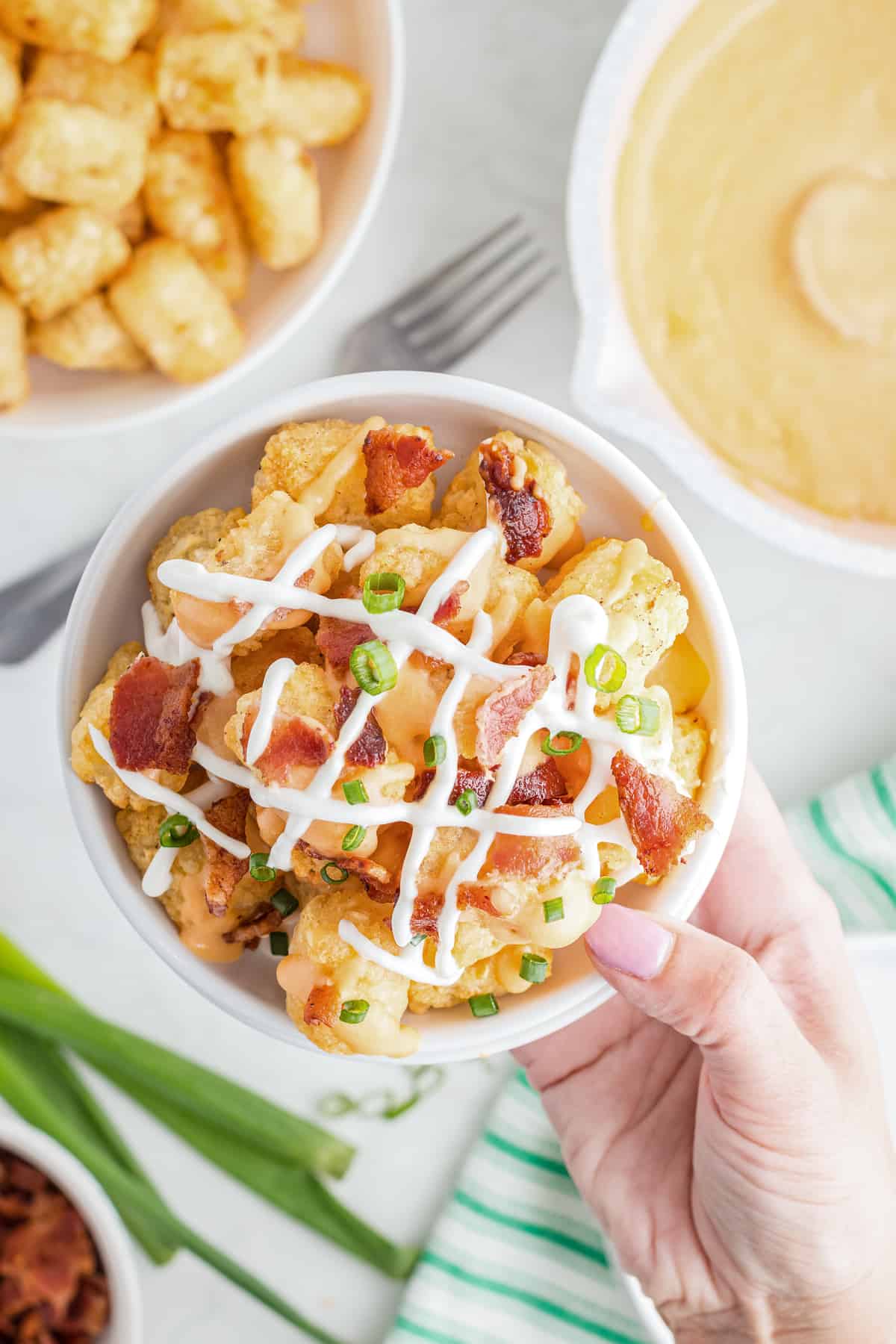 Hand picking up a bowl of loaded tater tots