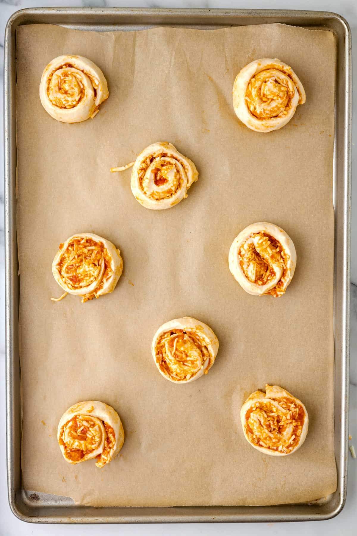 Sheet pan with parchment paper and pizza pinwheels before baking