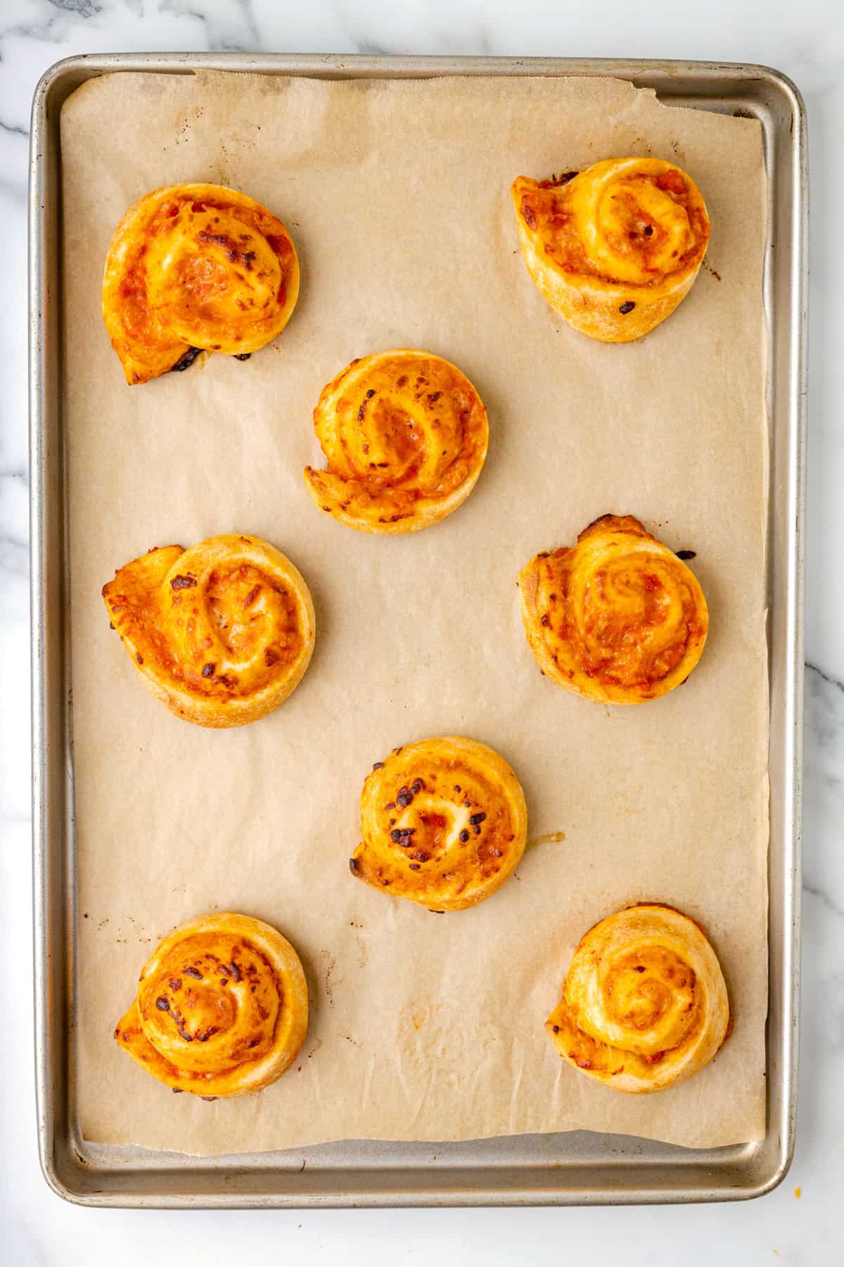 Sheet pan with parchment paper and baked pizza pinwheels