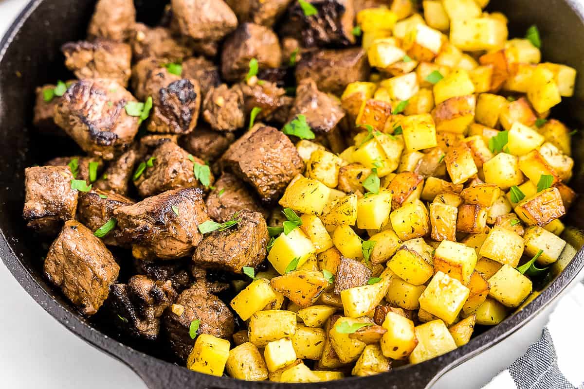 Cast iron skillet with steak pieces and potatoes