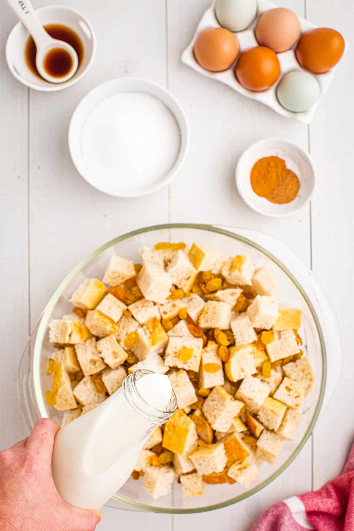 Pouring milk over pieces of bread in glass bowl