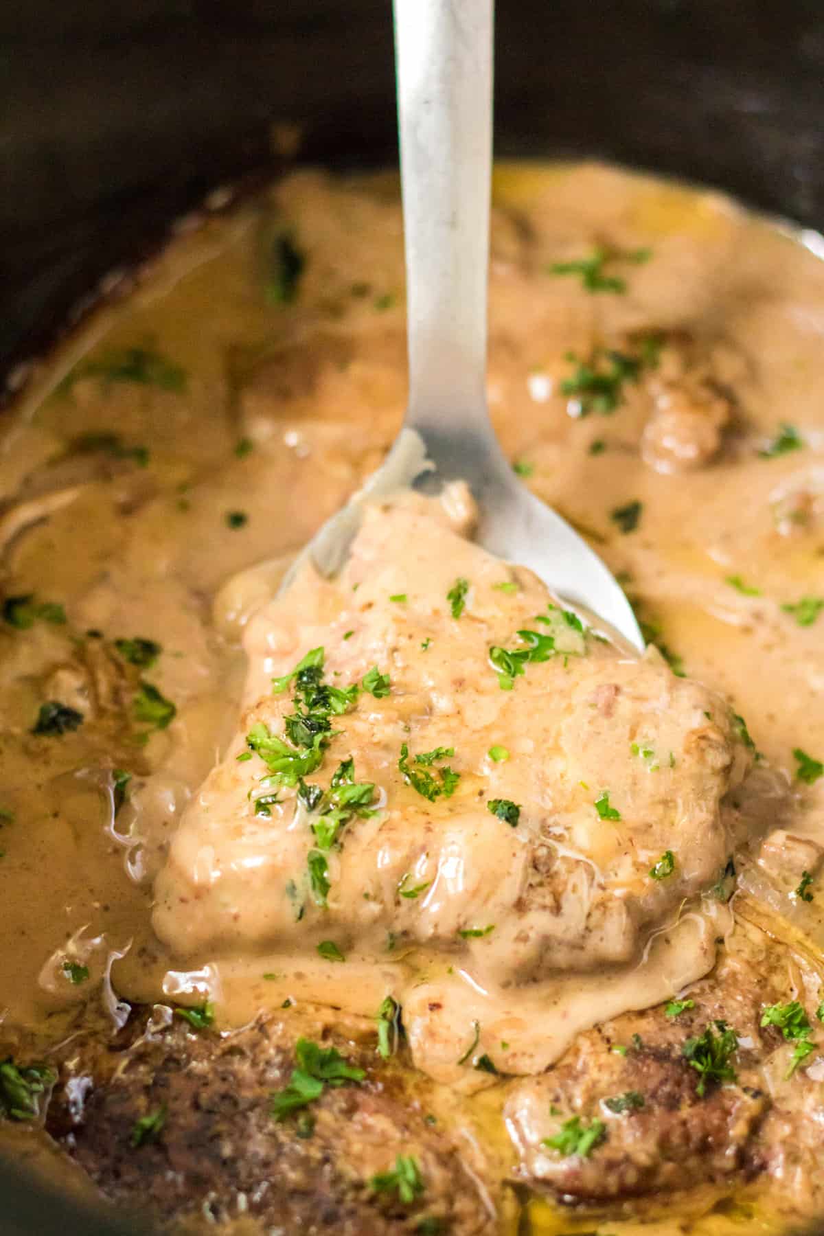 Spoon lifting cube steak out of crock pot