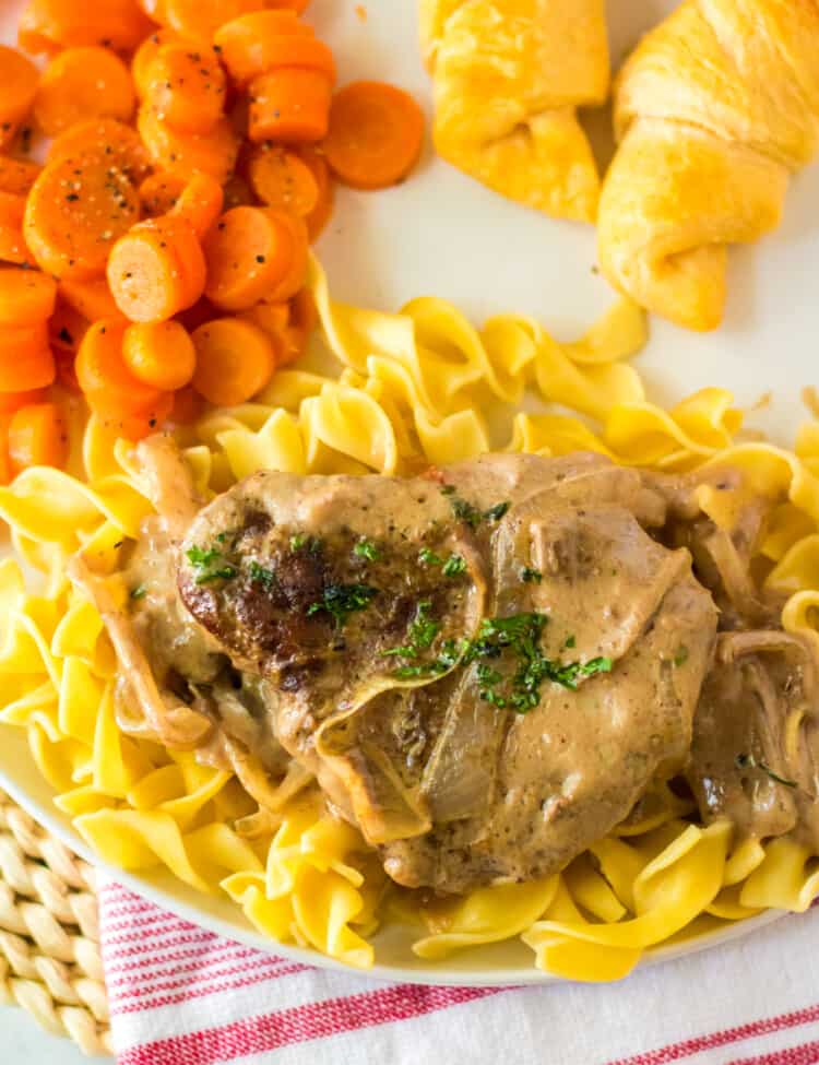 Cube steak served over a bed of egg noodles on white plate