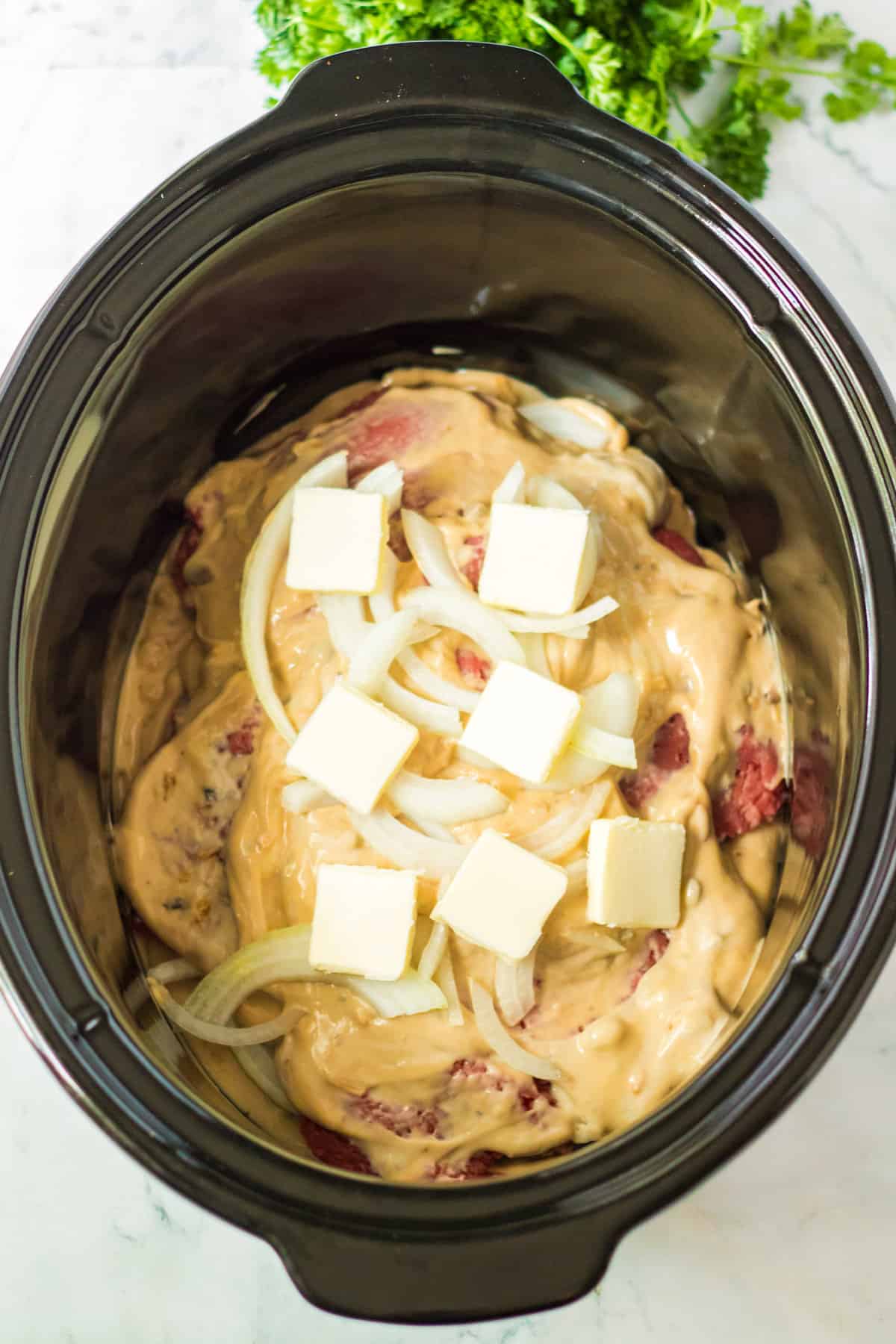 Black crock pot with butter and sliced onions over cube steak