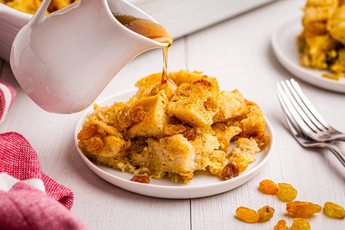 Pouring syrup over the top of bread pudding on white plate