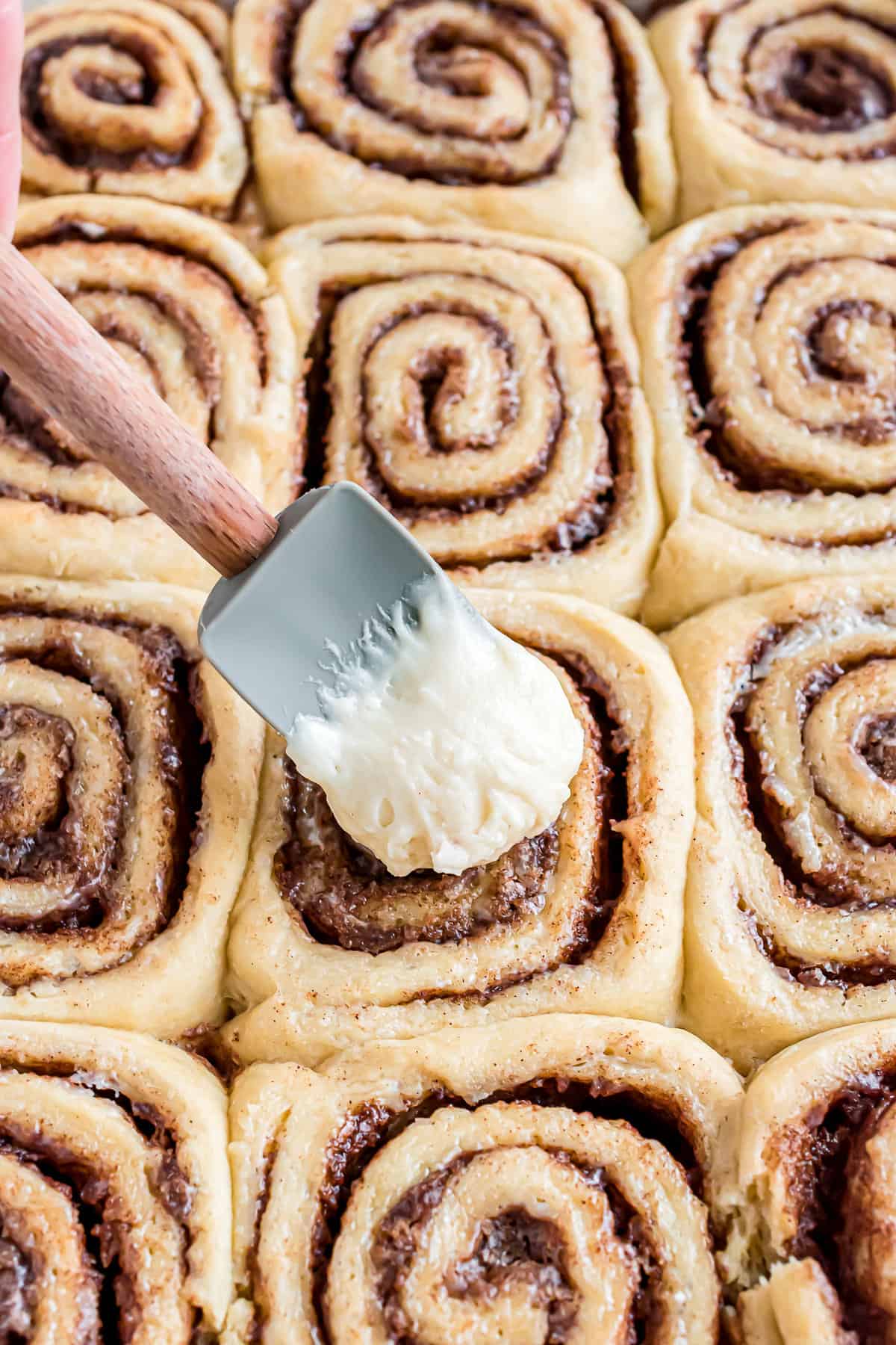 Putting cream cheese frosting on cinnamon roll