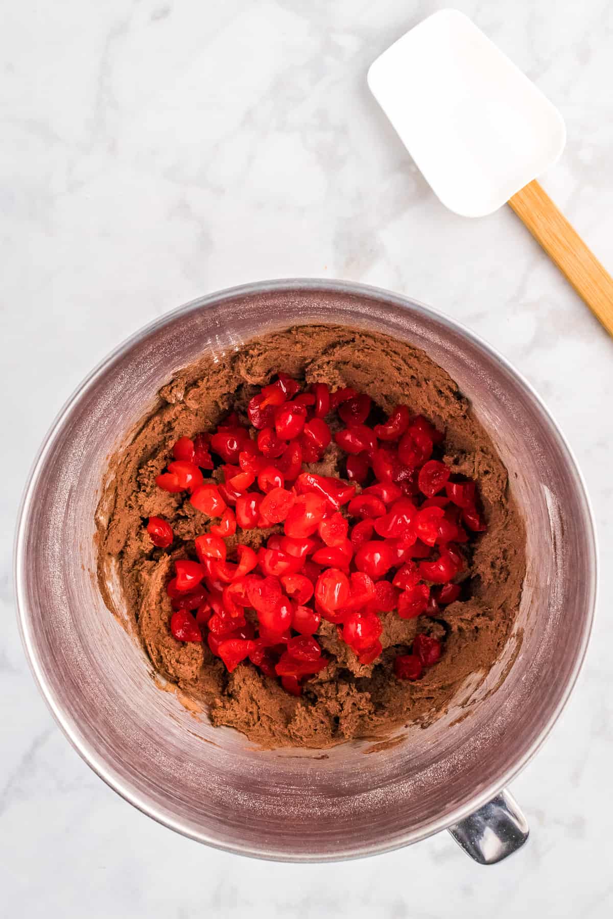 Overhead image of mixing bowl with chocolate cookie dough with chopped maraschino cherries