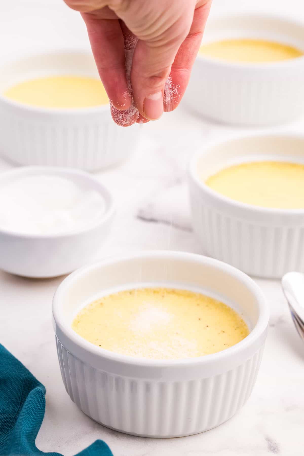 Sprinkling sugar on creme brulee in ramekin