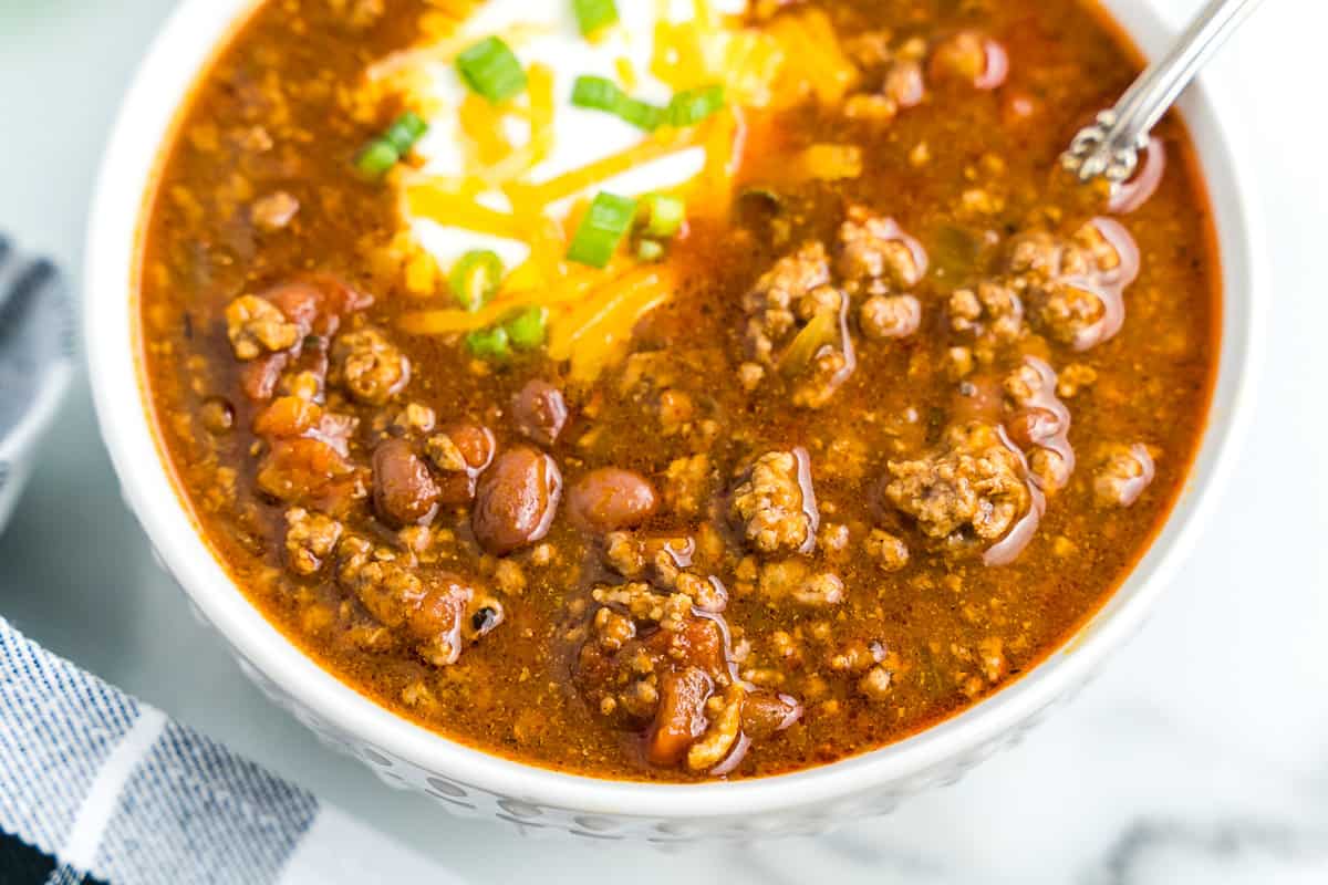 White bowl with chili in it topped with sour cream, green onions and cheese