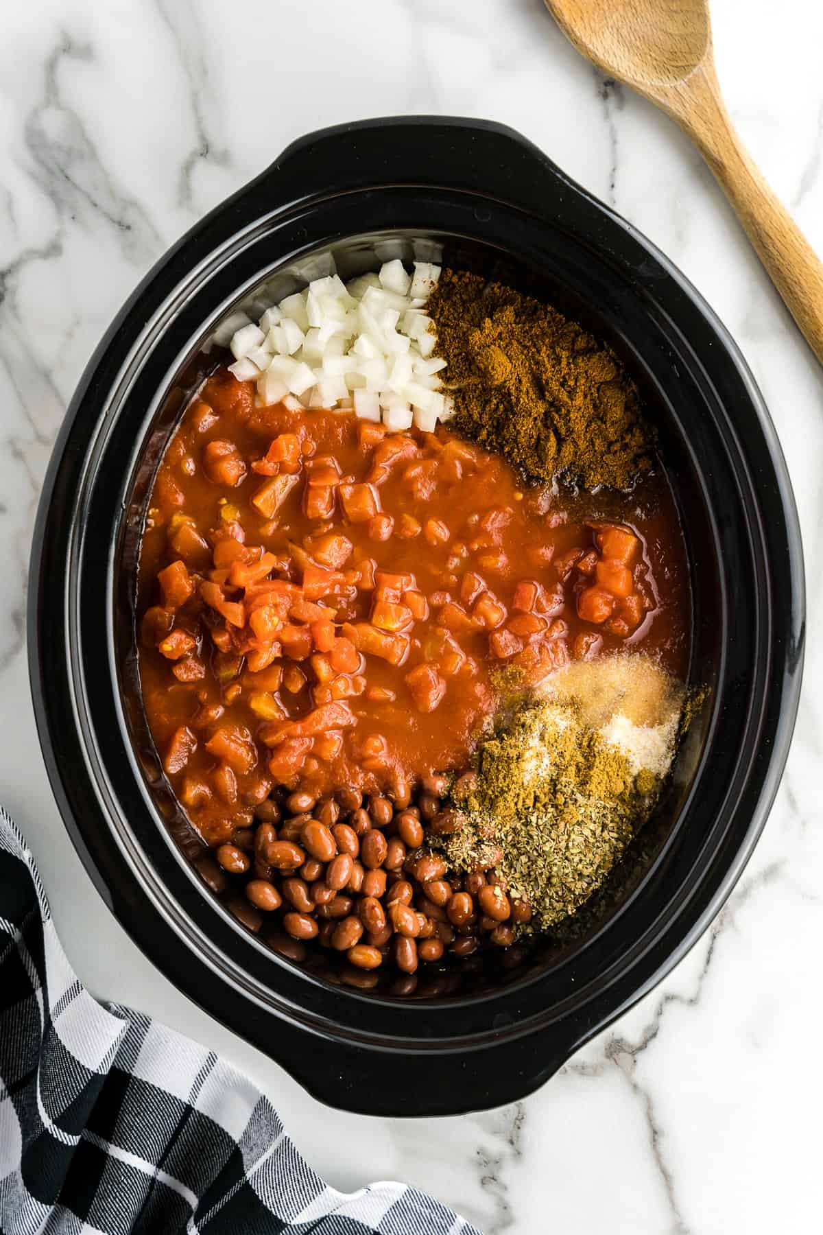 Black crock pot with chili ingredients before mixing