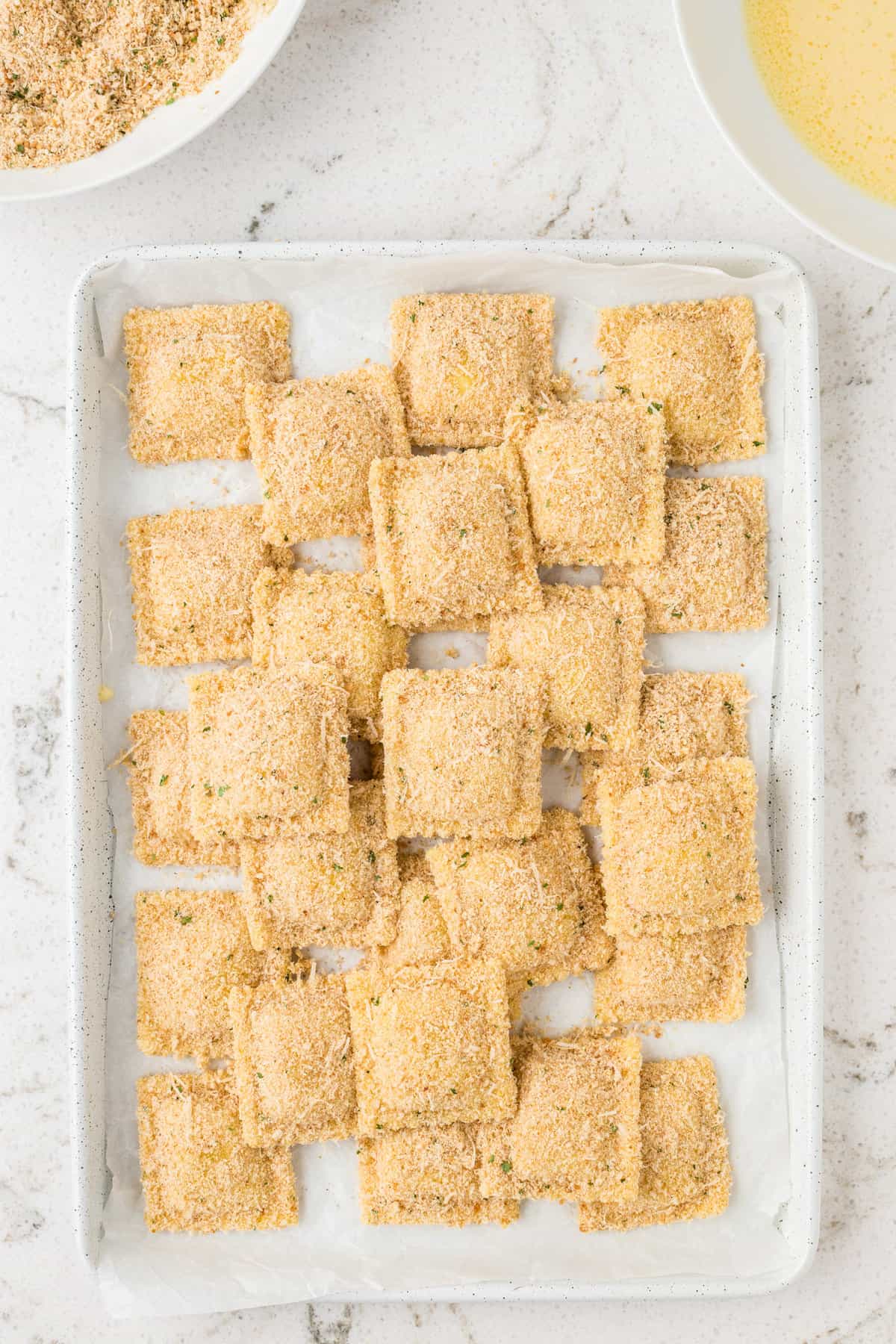 Overlead of uncooked breaded ravioli on baking sheet