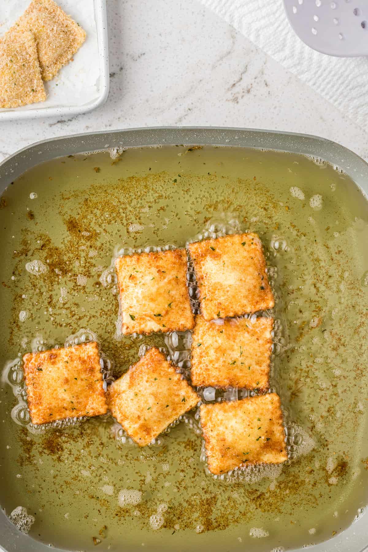 Overhead of breaded ravioli in oil mixture