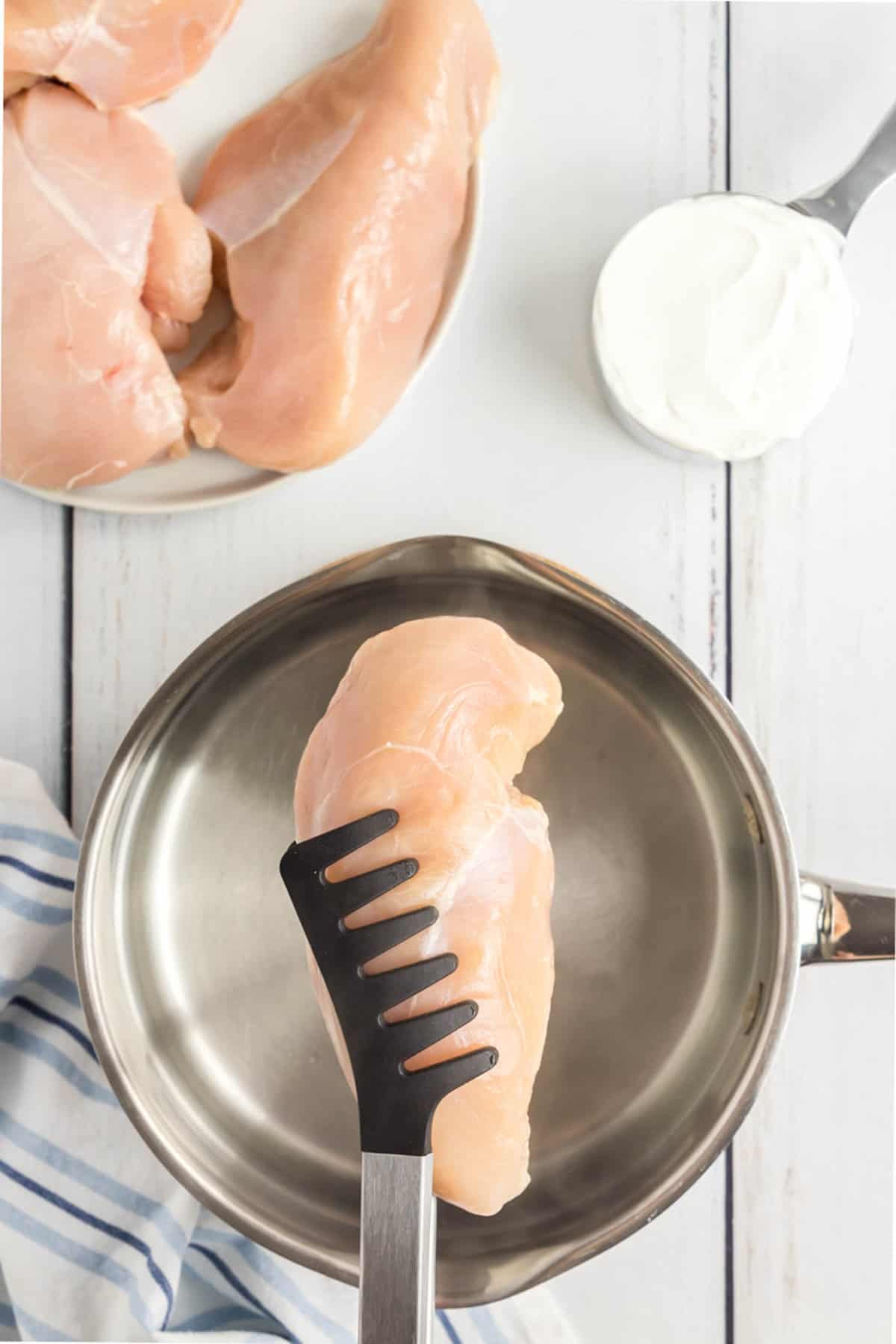 Lifting chicken breast into water in saucepan