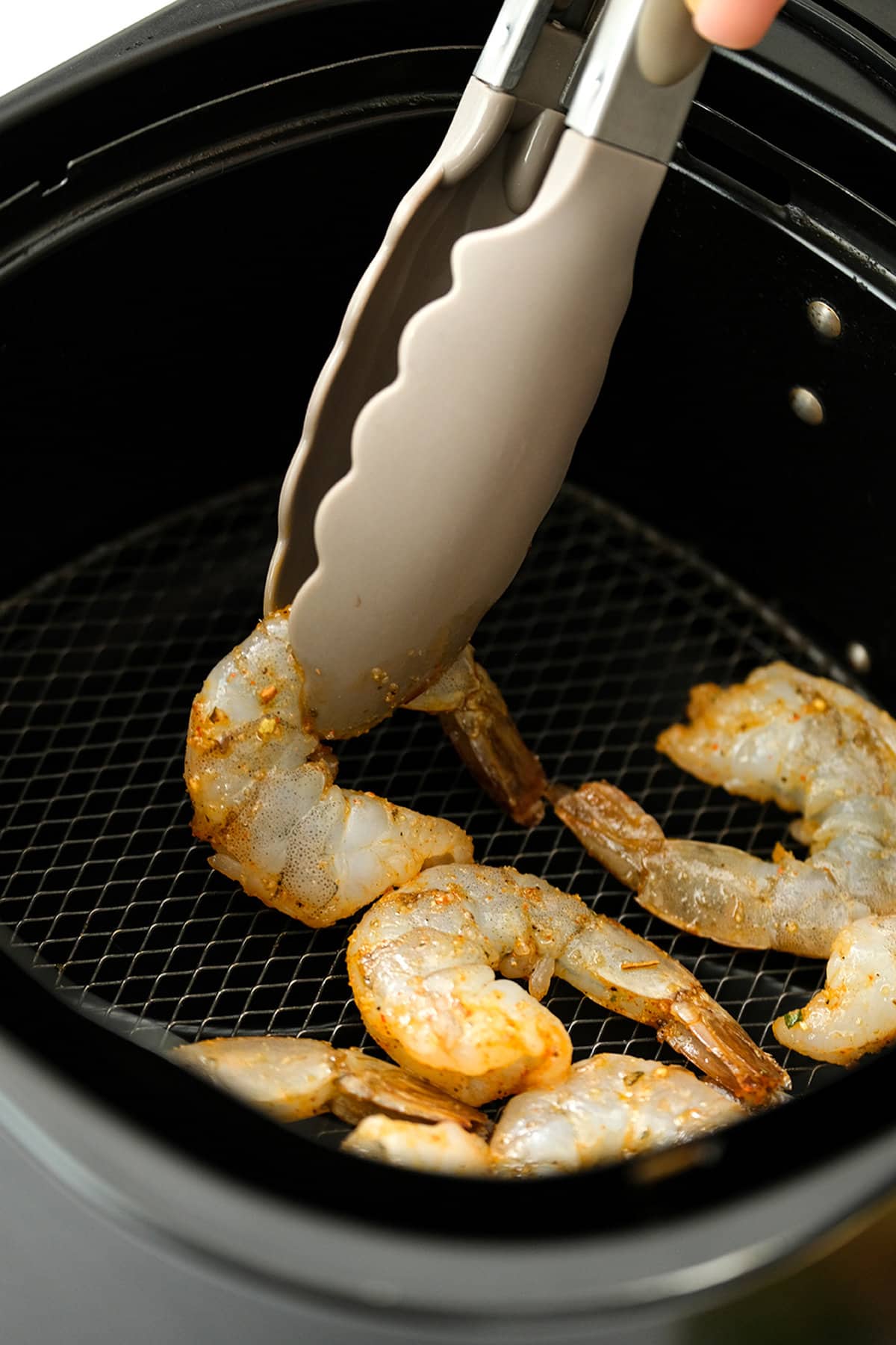 Placing shrimp in air fryer basket with tong