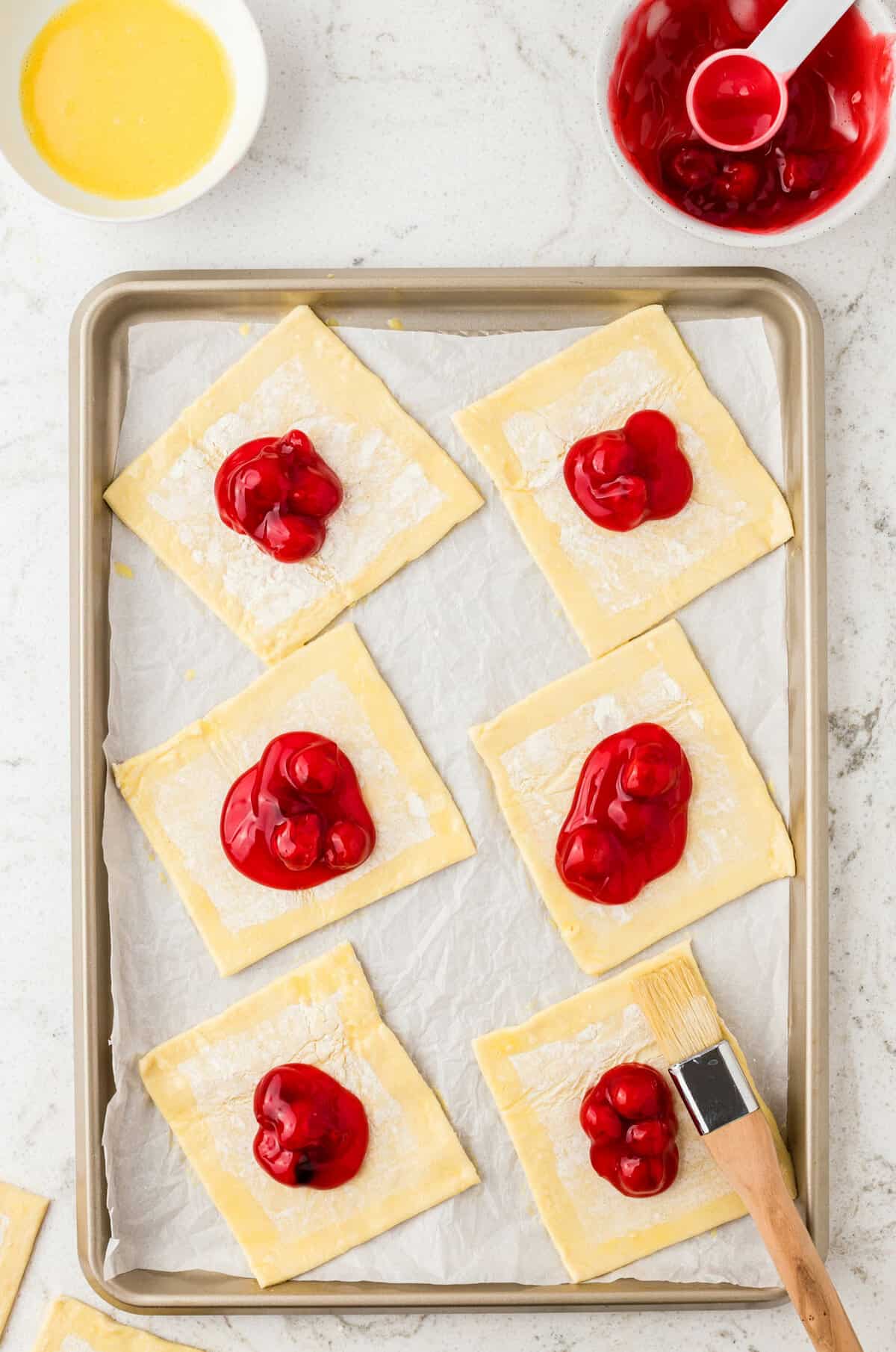 Unbaked Square Pastries with Cherry Pie Filling on Baking Sheet