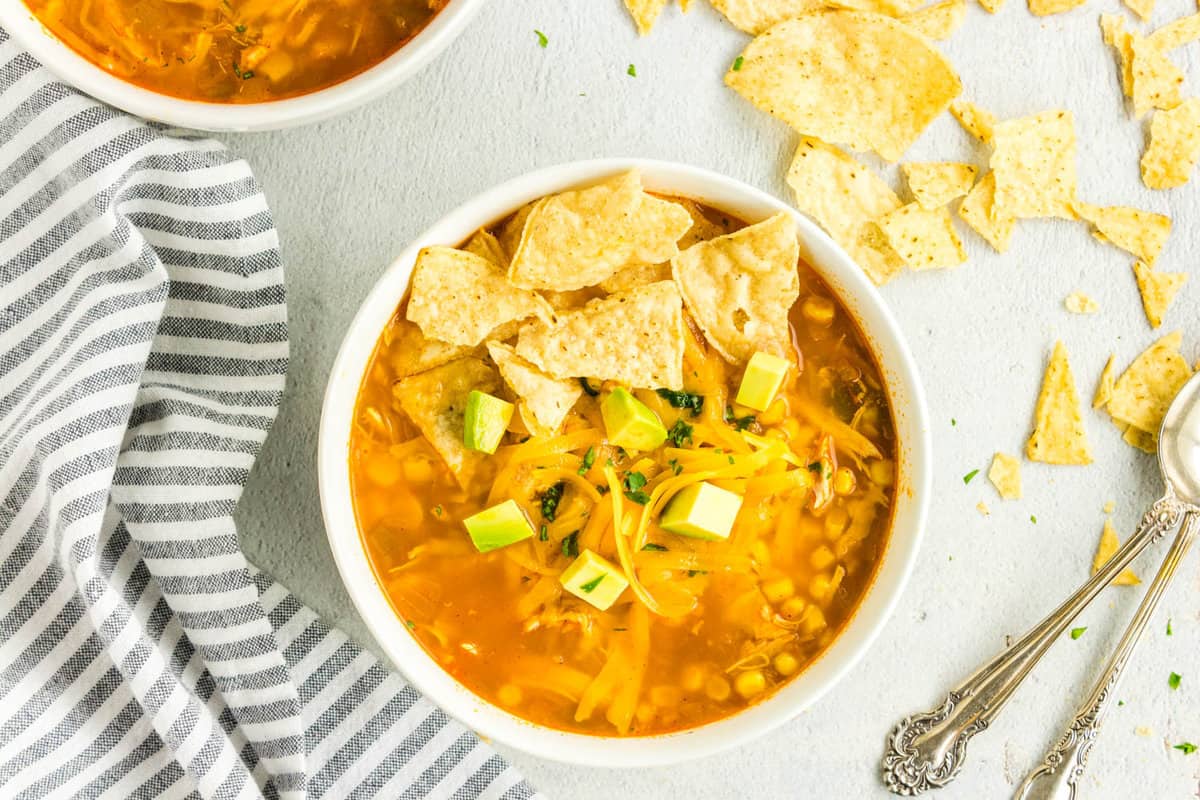 Easy Chicken Tortilla Soup Recipe in a Bowl Topped with Chips, Cheese, and Avacados