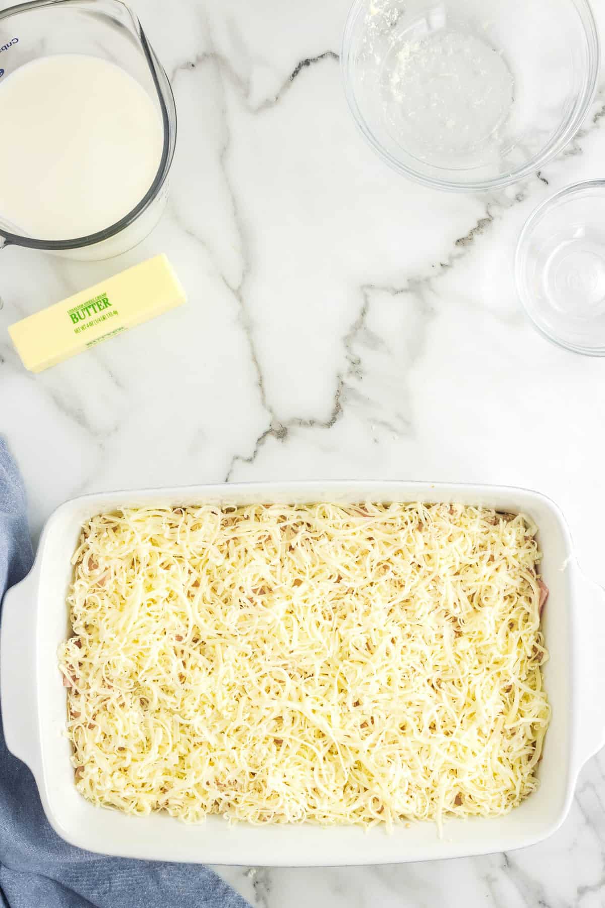 Topping Meat Layers with Shredded Cheese for Chicken Cordon Bleu Casserole