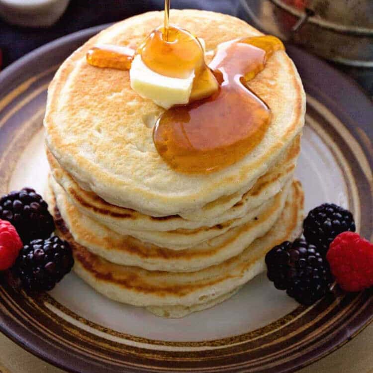 Stack of pancakes on plate with butter and syrup