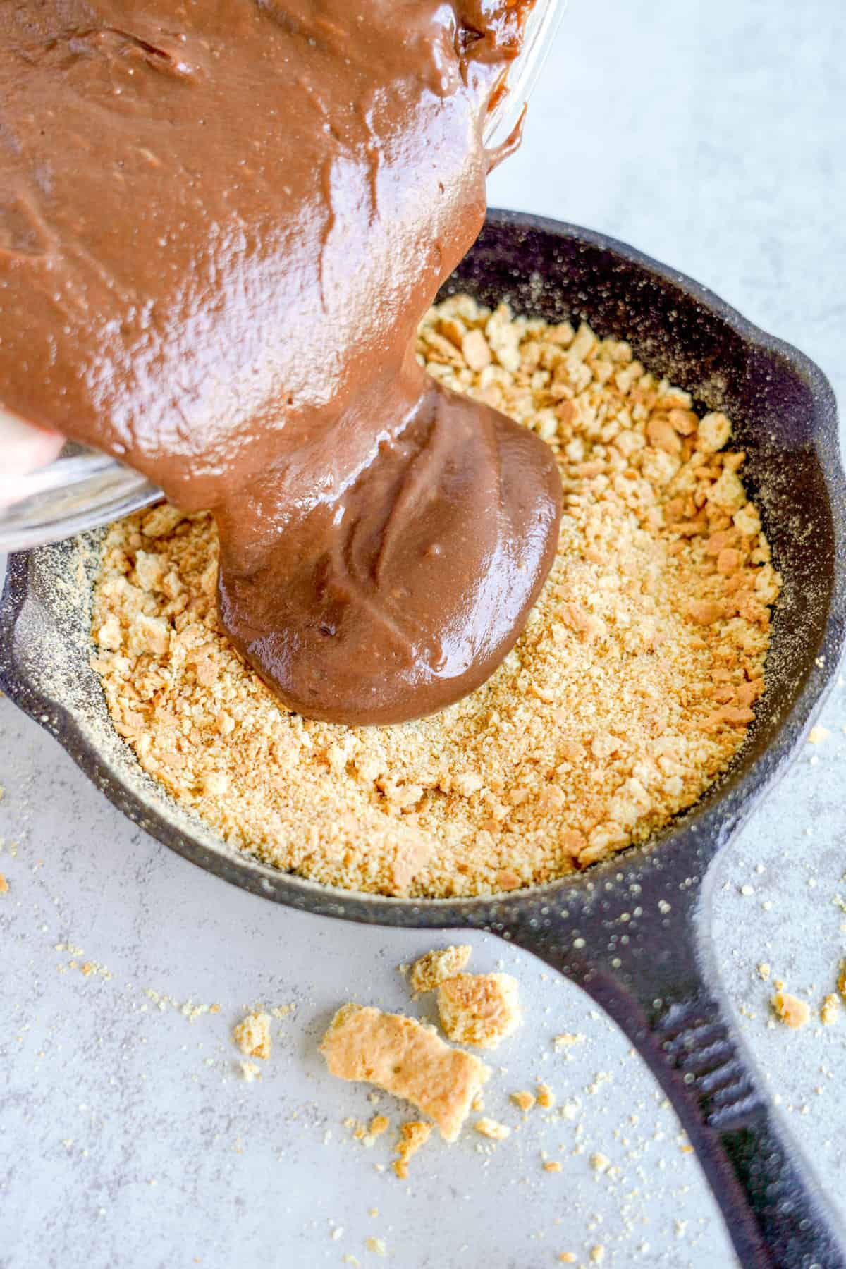 Pouring Mixture Over Graham Cracker Crust in Cast Iron Skillet