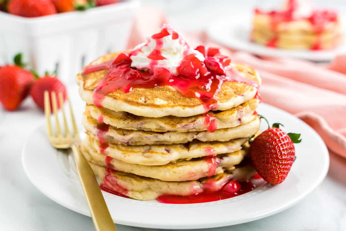 Strawberry Pancake Recipe on Plate Topped with Strawberry Syrup and Whipped Cream