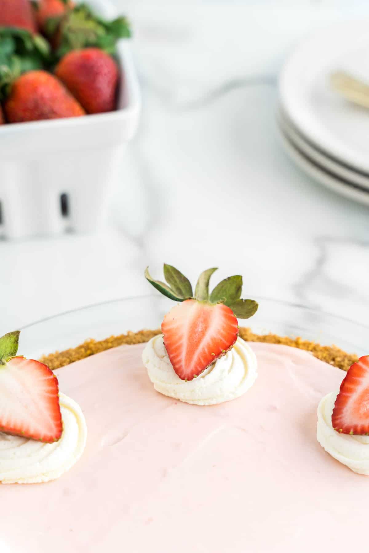 Garnishing No Bake Strawberry Cheesecake with Whipped Cream Dollop and Fresh Strawberry