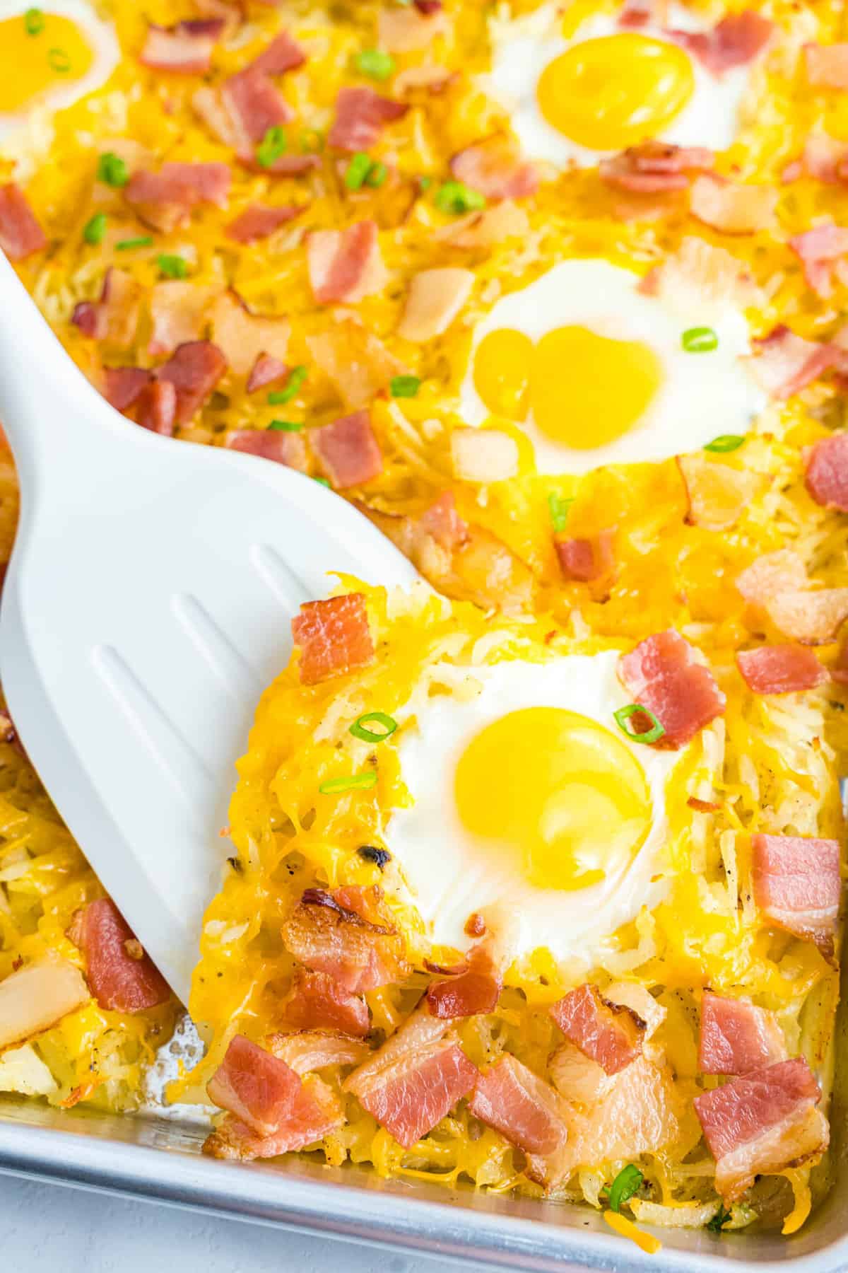 Spoon scooping an egg off a sheet pan breakfast