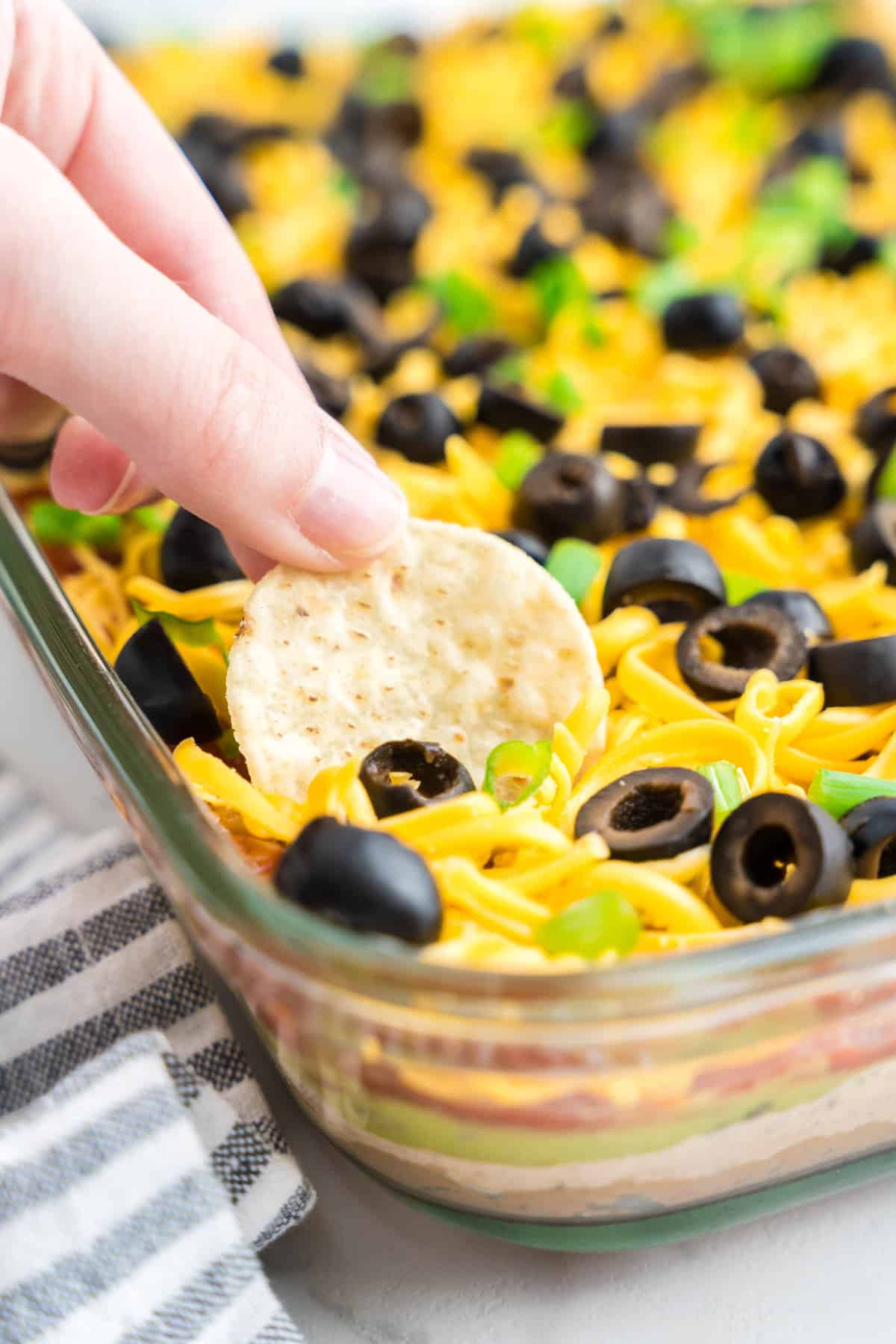 Using tortilla chip as a dipper for seven layer taco dip in glass serving dish