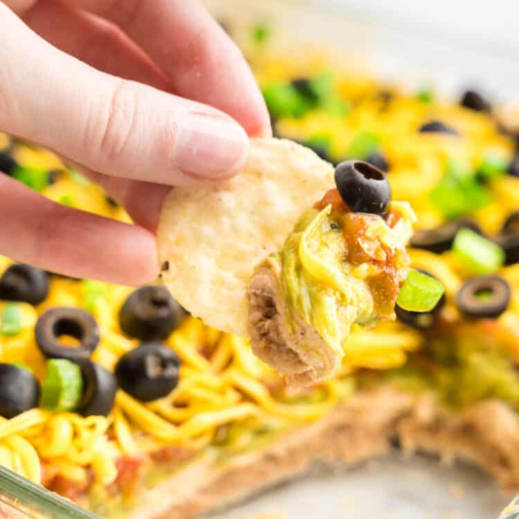 7 Layer Taco Dip in Serving Dish Using Tortilla Chip to Dip
