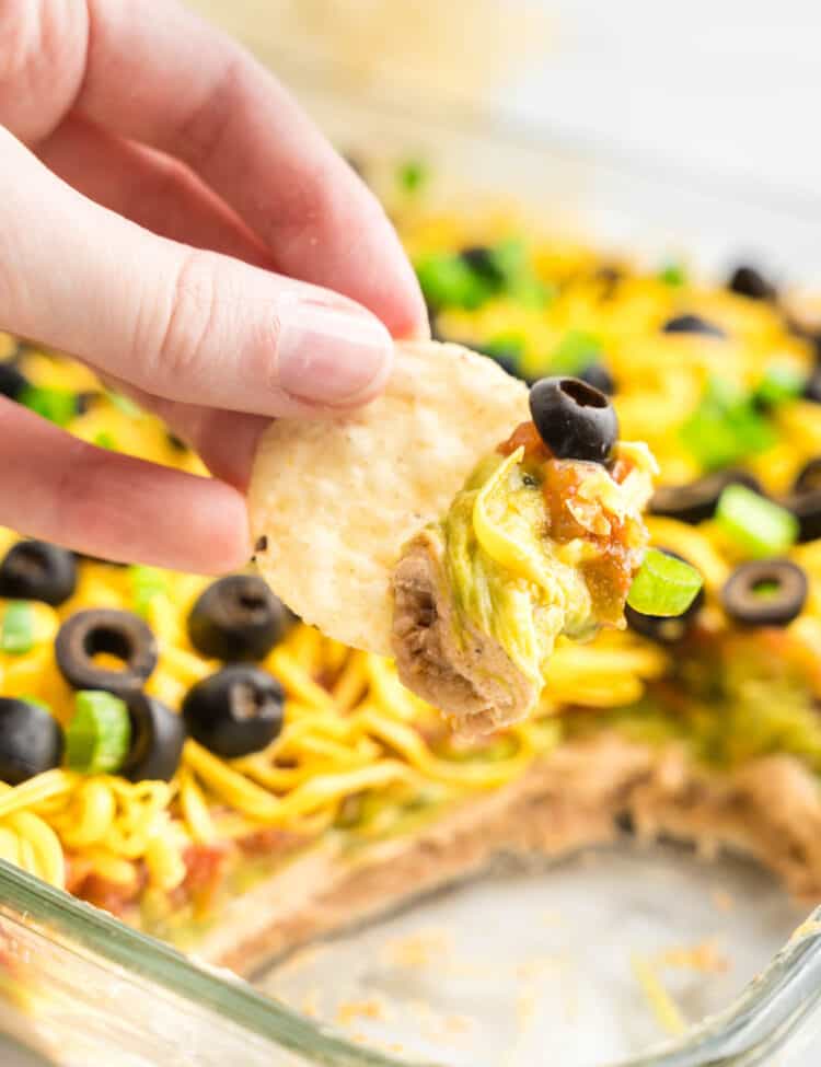 7 Layer Taco Dip in Serving Dish Using Tortilla Chip to Dip