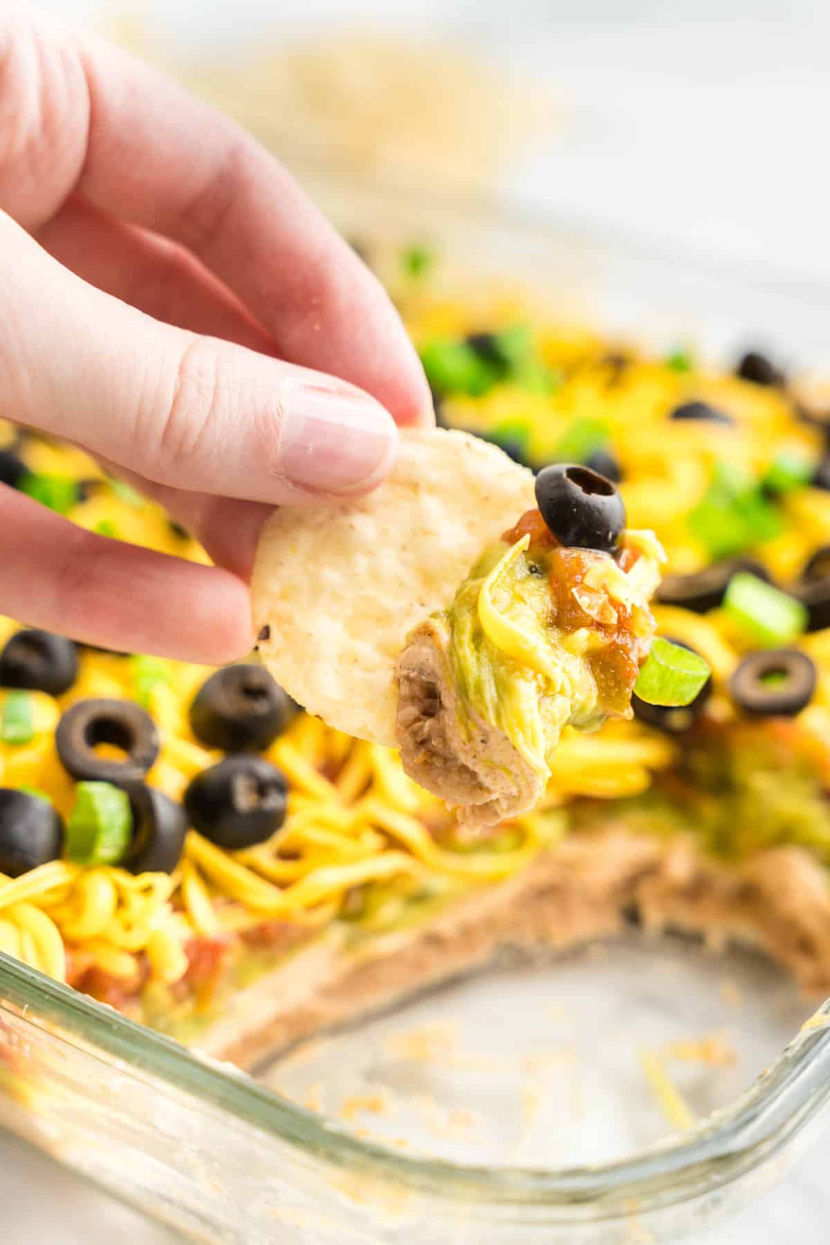 7 Layer Taco Dip in Serving Dish Using Tortilla Chip to Dip