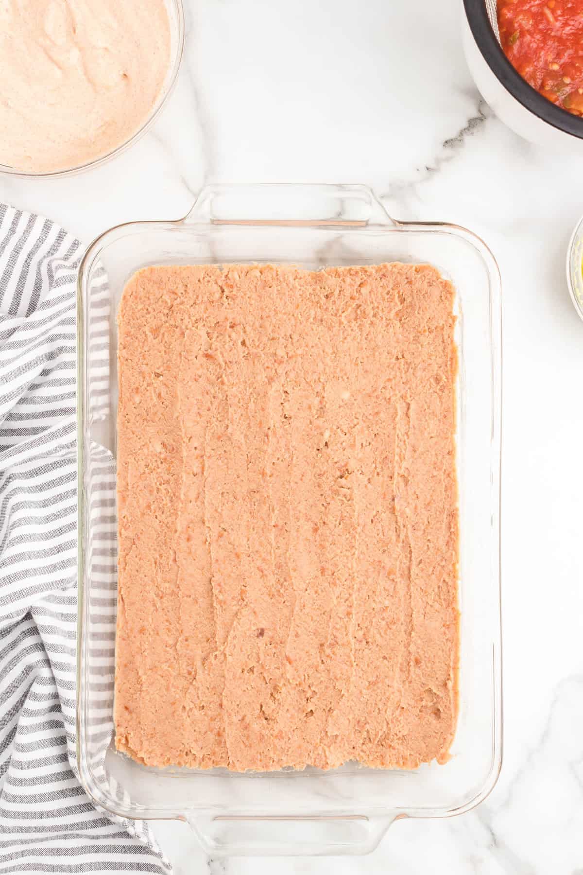 Spreading refried beans in glas serving dish for taco layer dip