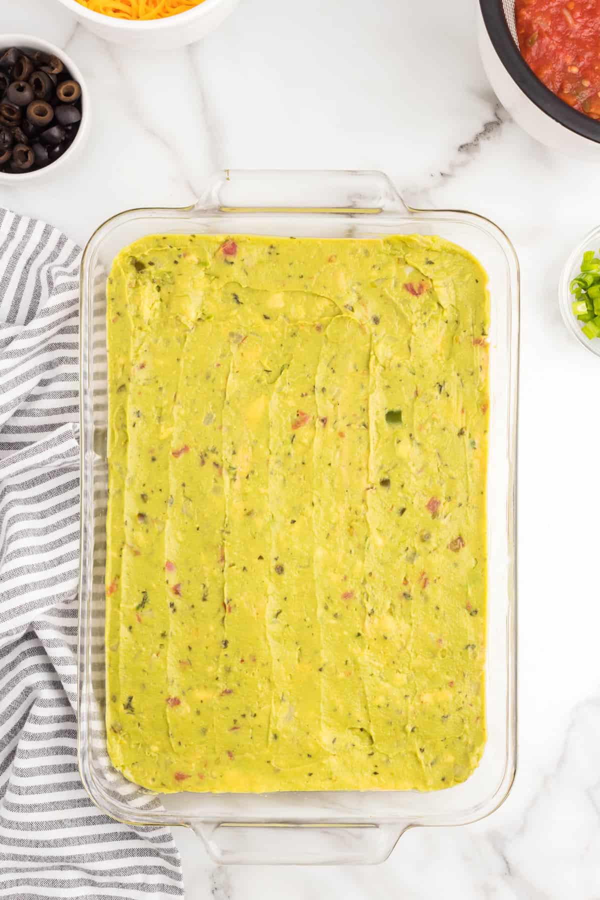 Guacamole spread evenly over refried beans for seven layer taco dip