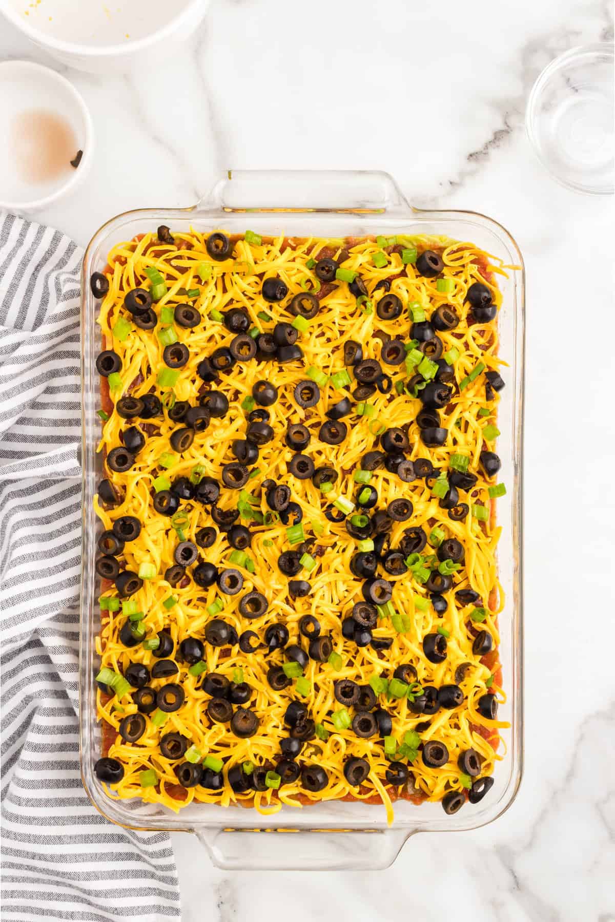 Topping 7 layer dip with sliced black olives and chopped green onion in glass serving dish