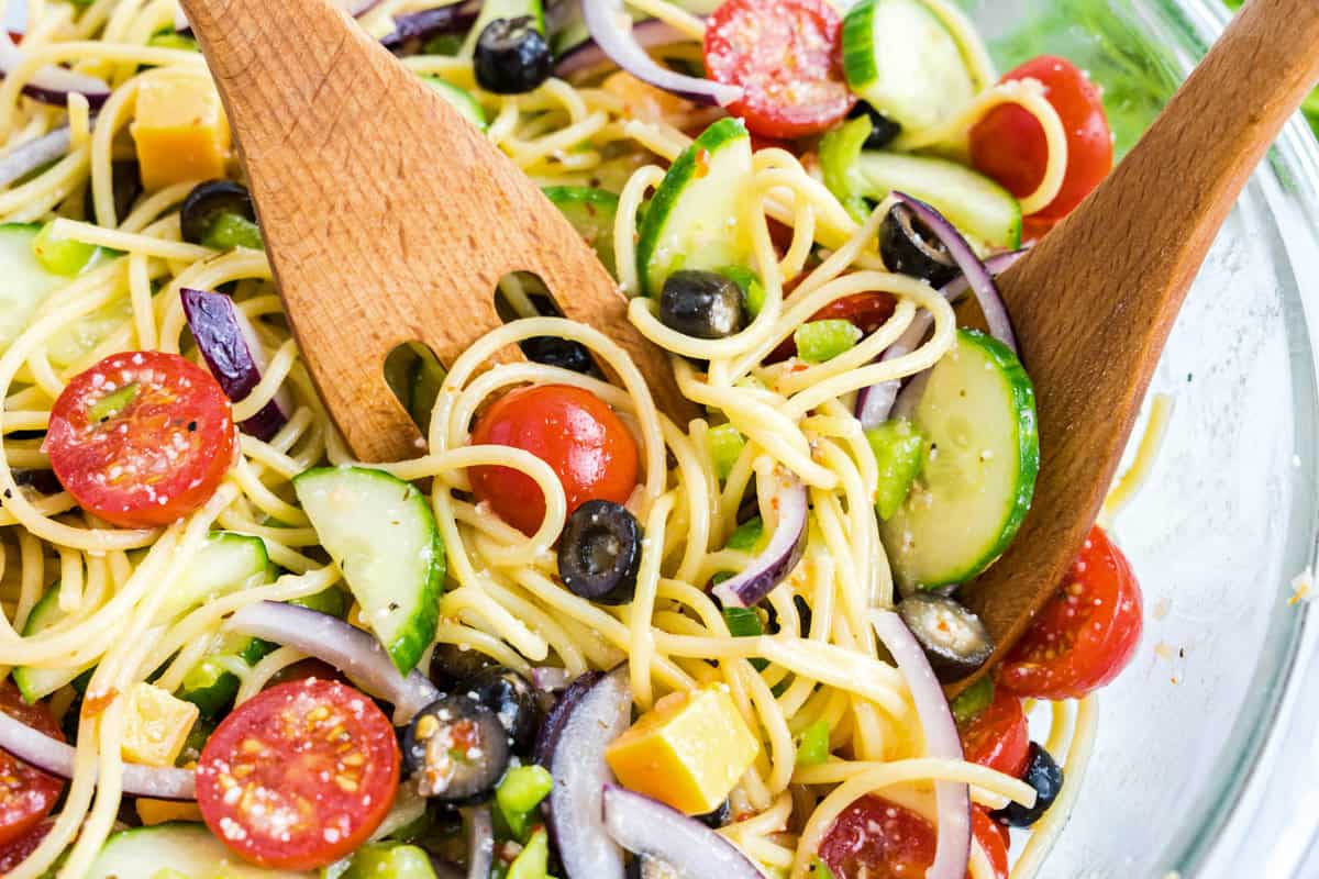 Tossing Pasta Salad with Italian Dressing in a bowl with a wooden spoon