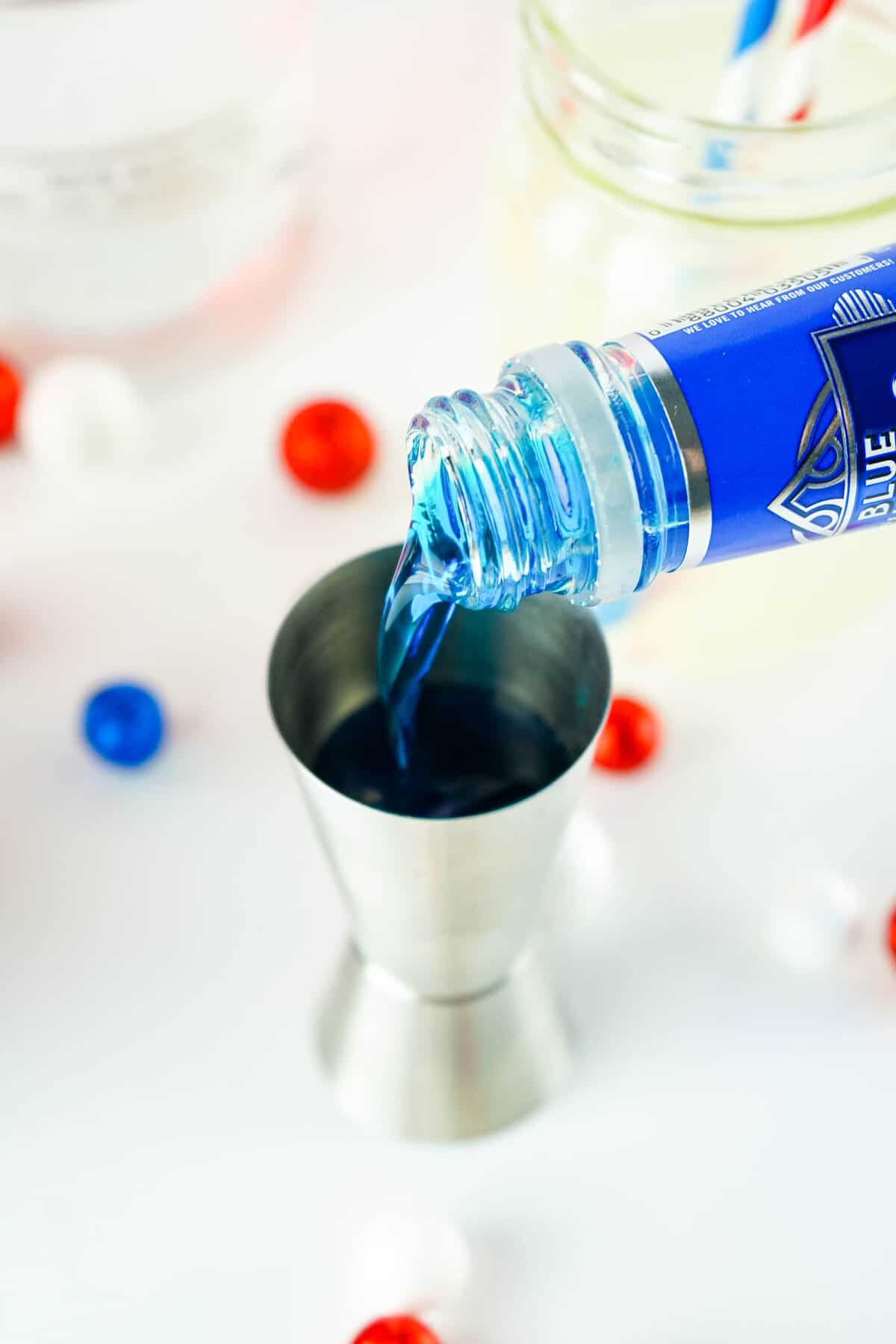 Pouring Blue Curacao into shot glass for Red White and Blue Layered Cocktail Recipe