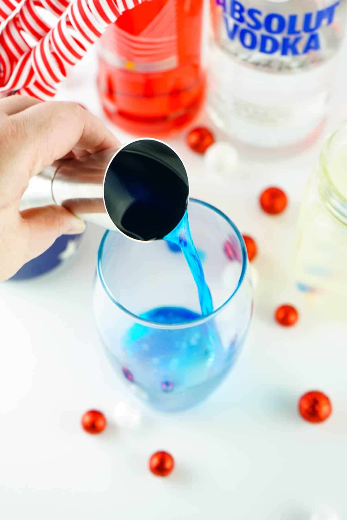 Pouring Blue Curacao from the shot glass in Glass for Red White and Blue Layered Cocktail Recipe
