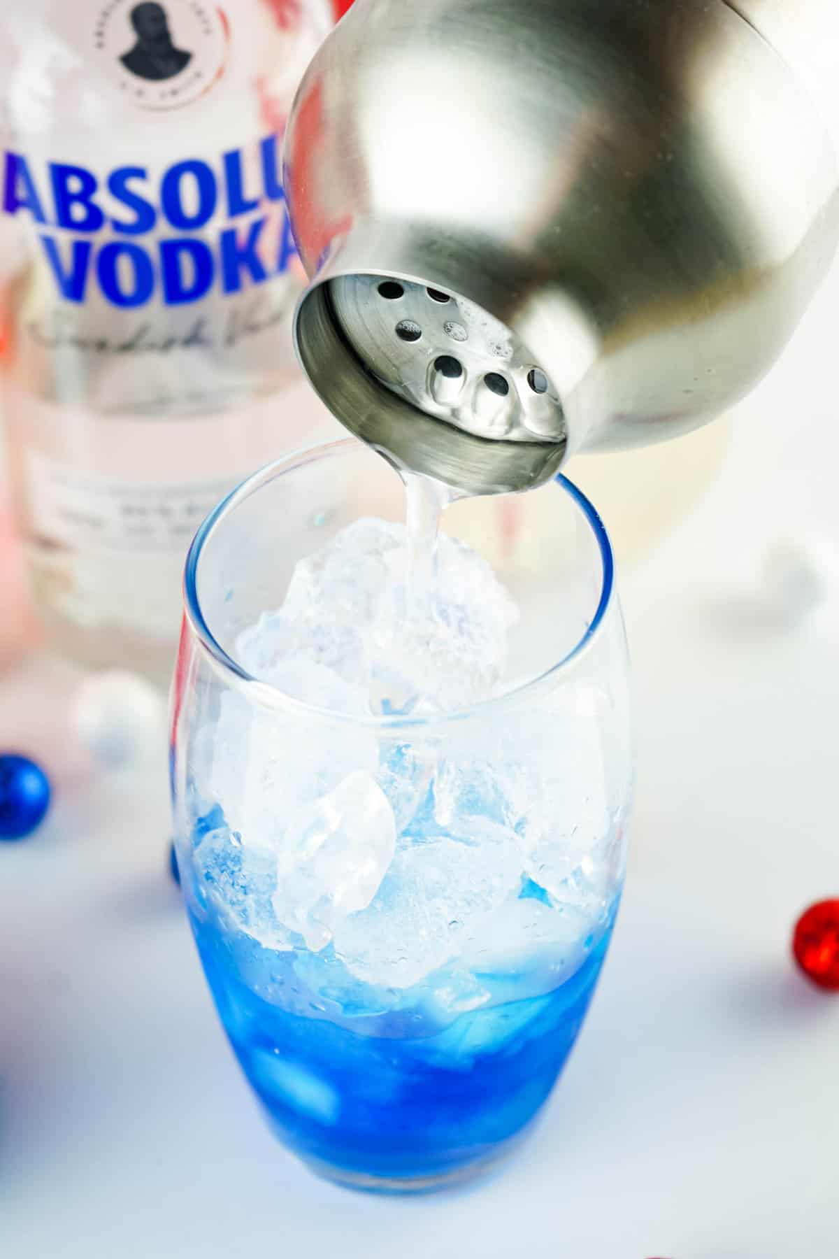 Using shaker to pour lemonade and vodka mixure into glass for Red, White and Blue Cocktail
