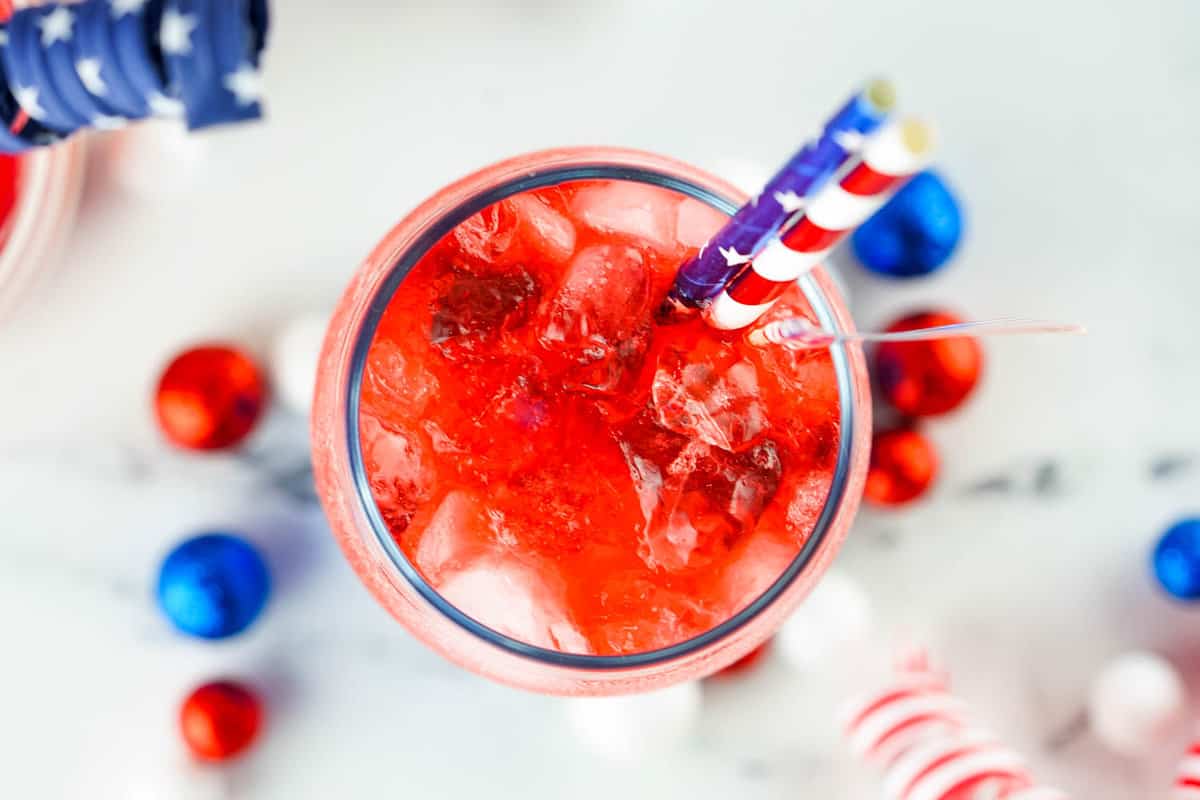 Adding festive straws and flags to Red White and Blue Layered Cocktail drink for a fun touch